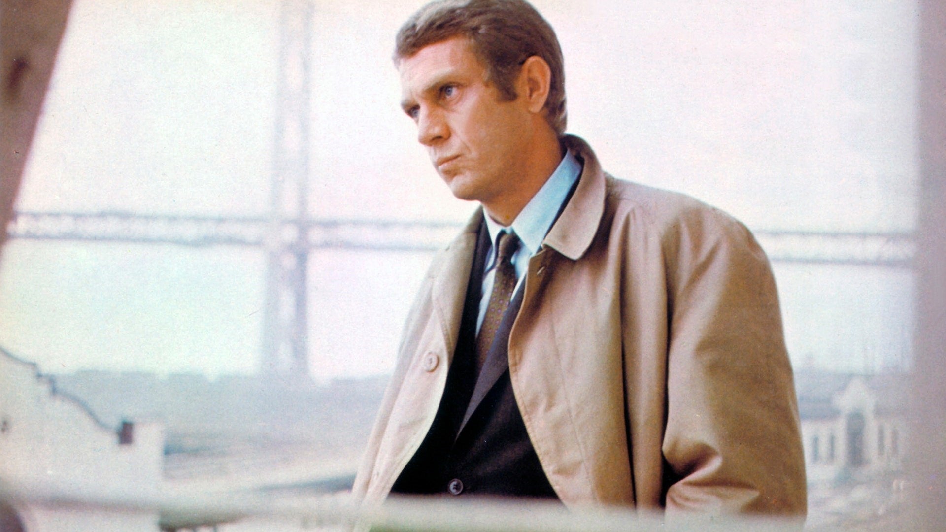 Steve McQueen wearing a beige tan raincoat and ancient madder tie in Bullitt