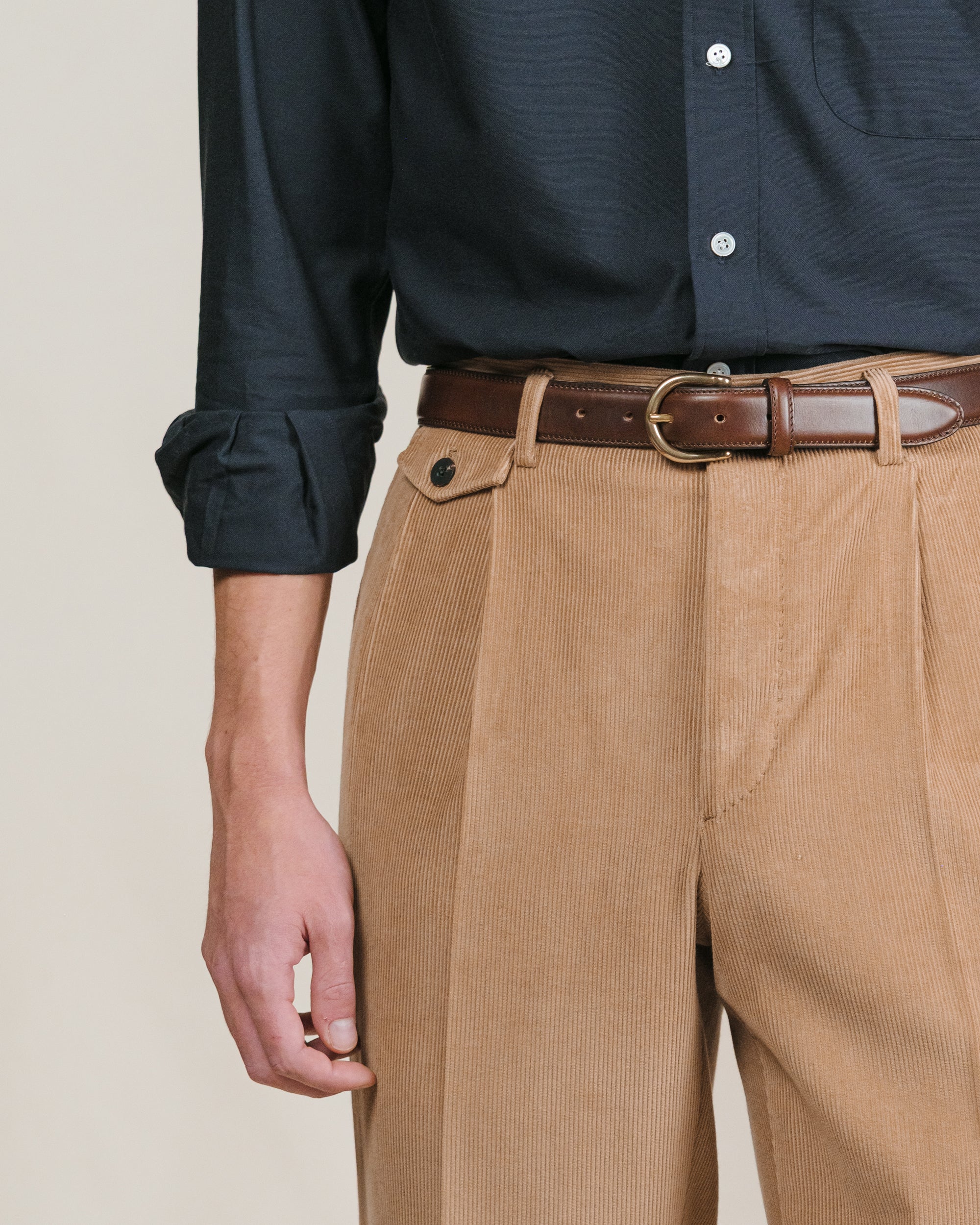 Person wearing a navy shirt and light brown corduroy trousers with a brown leather belt with brass buckle