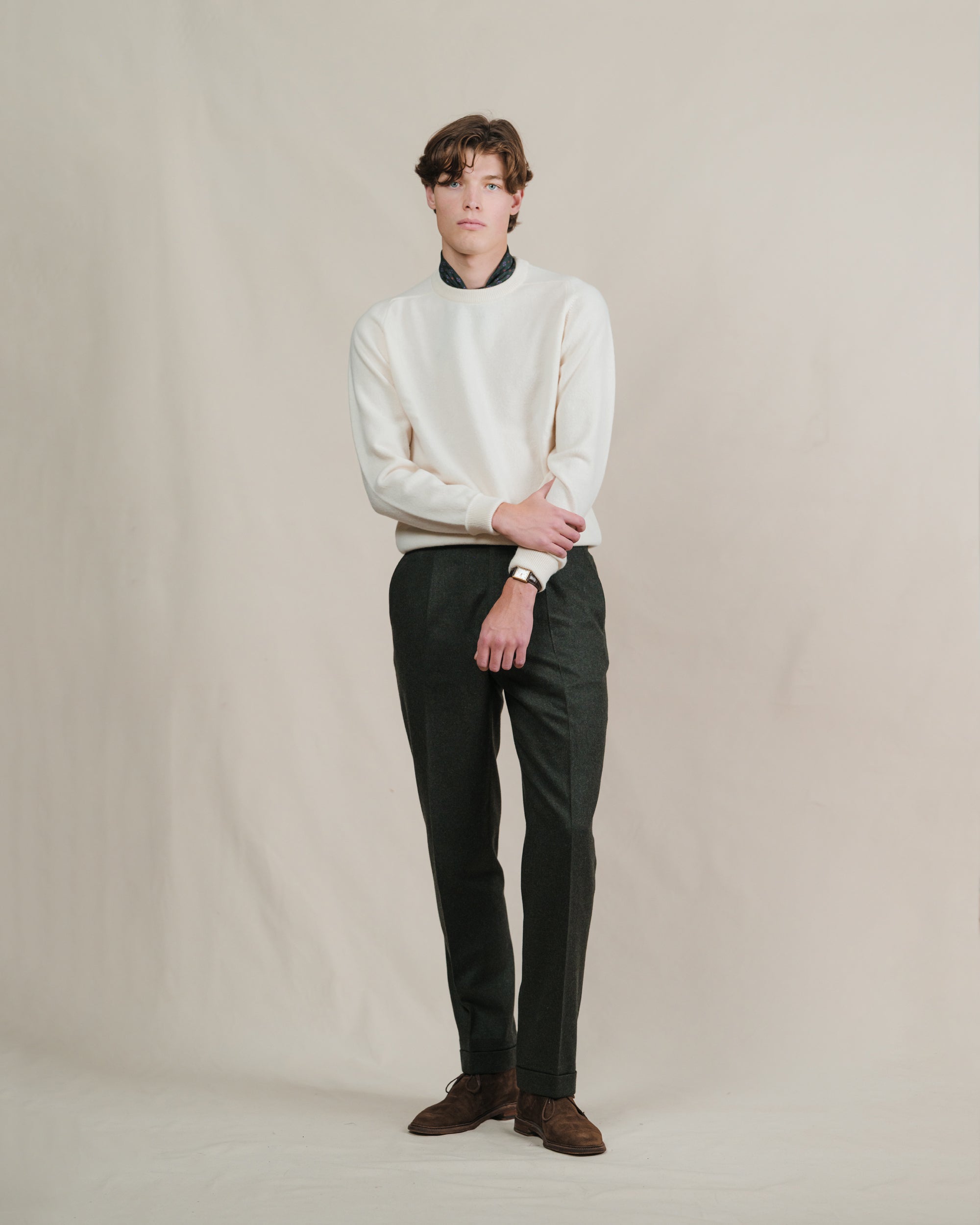 Man wearing dark green flannel trousers with an ecru crewneck sweater and brown suede chukkah boots