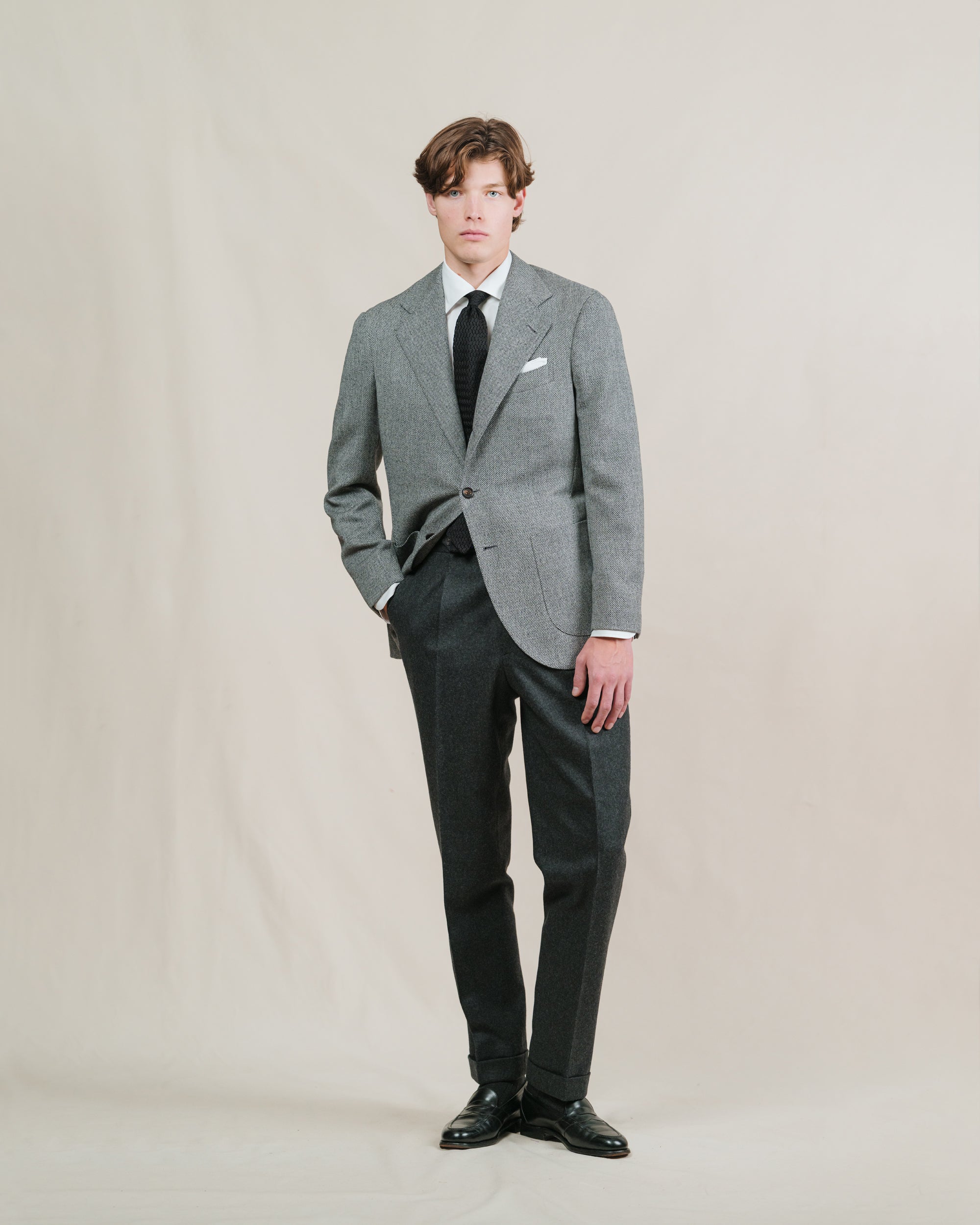 Man wearing a pair of charcoal flannel trousers, a grey broken twill sport coat, white shirt and black zigzag knitted tie