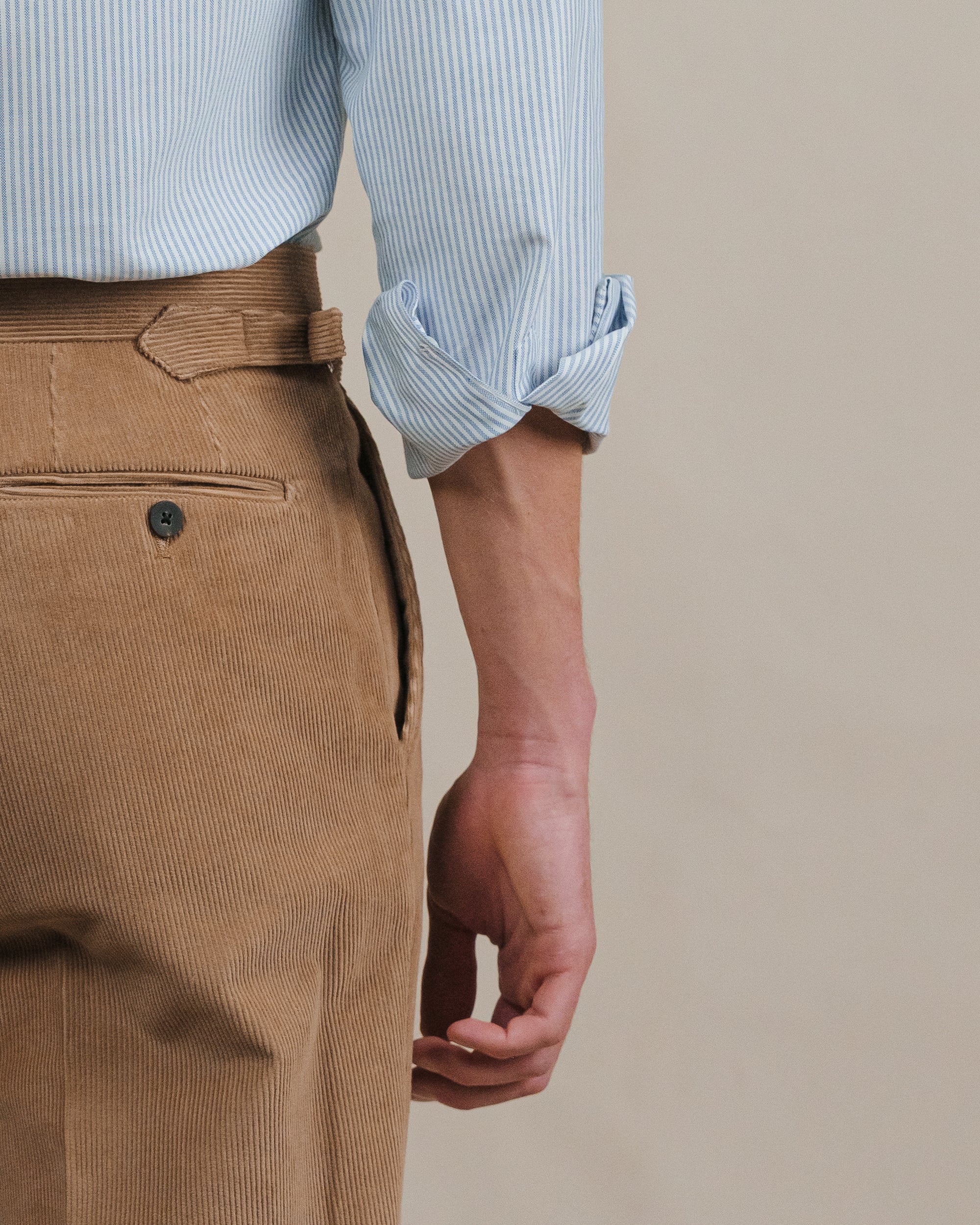 Person wearing a light blue striped shirt and camel brown corduroy pants on a beige background