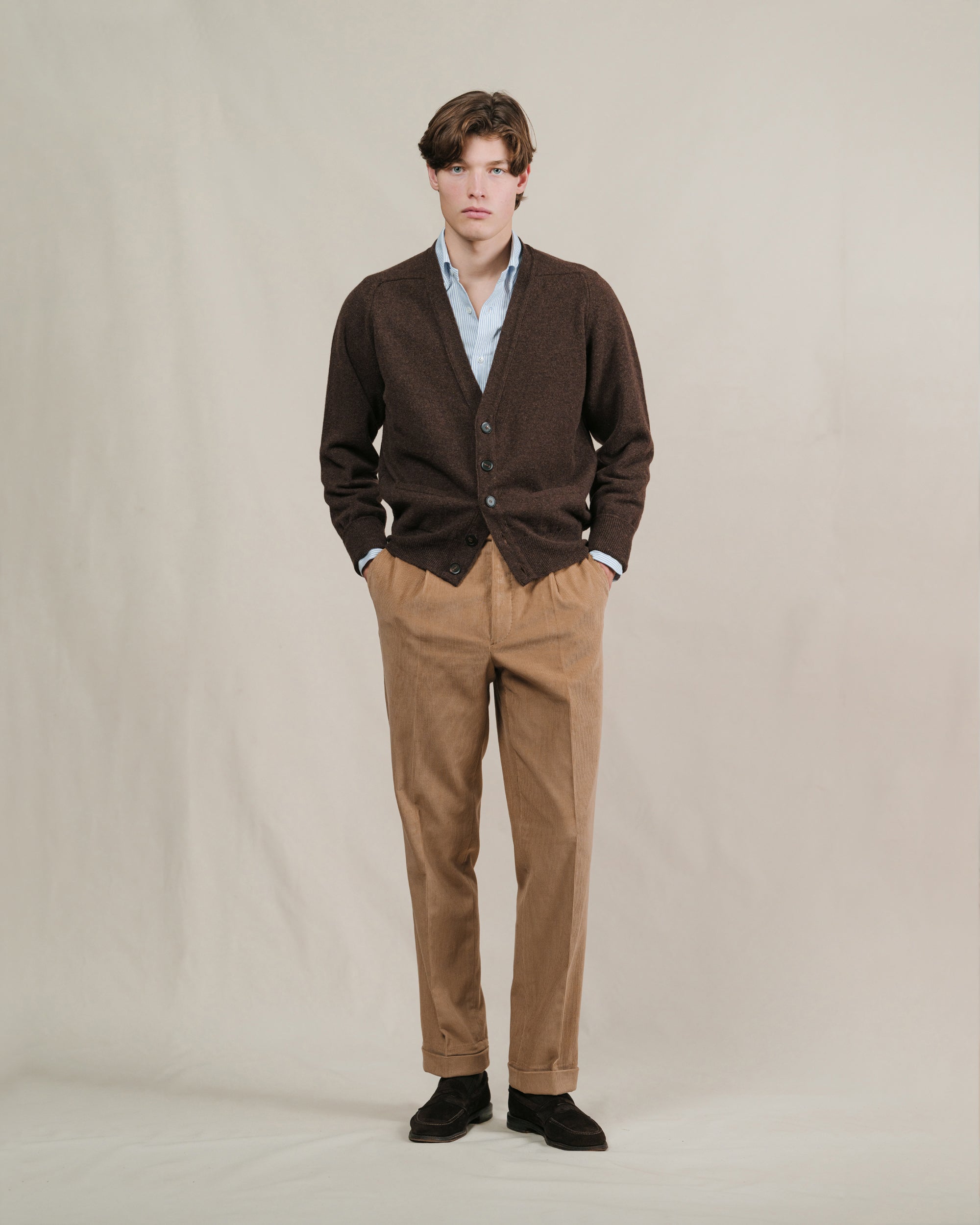 Man wearing a brown cardigan, light blue striped shirt, tan corduroy trousers and brown suede penny loafers