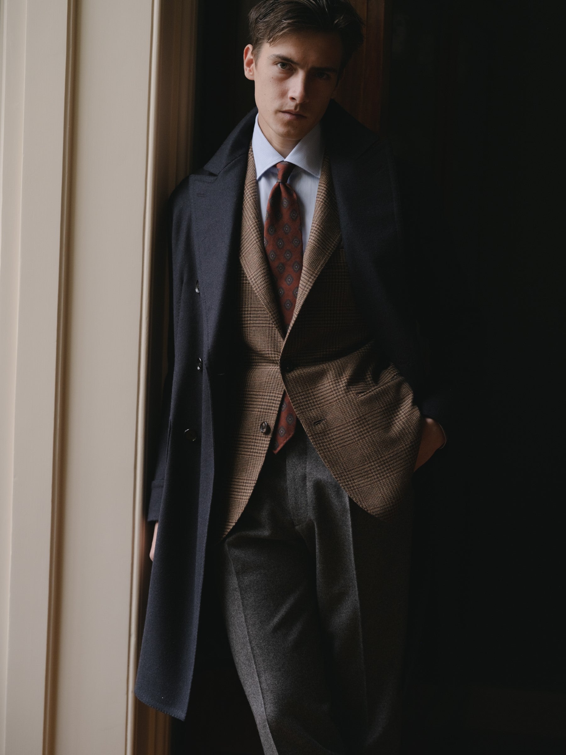 Man wearing a navy polo coat, brown prince of wales sport coat, light blue bengal stripe shirt and rust ancient madder tie