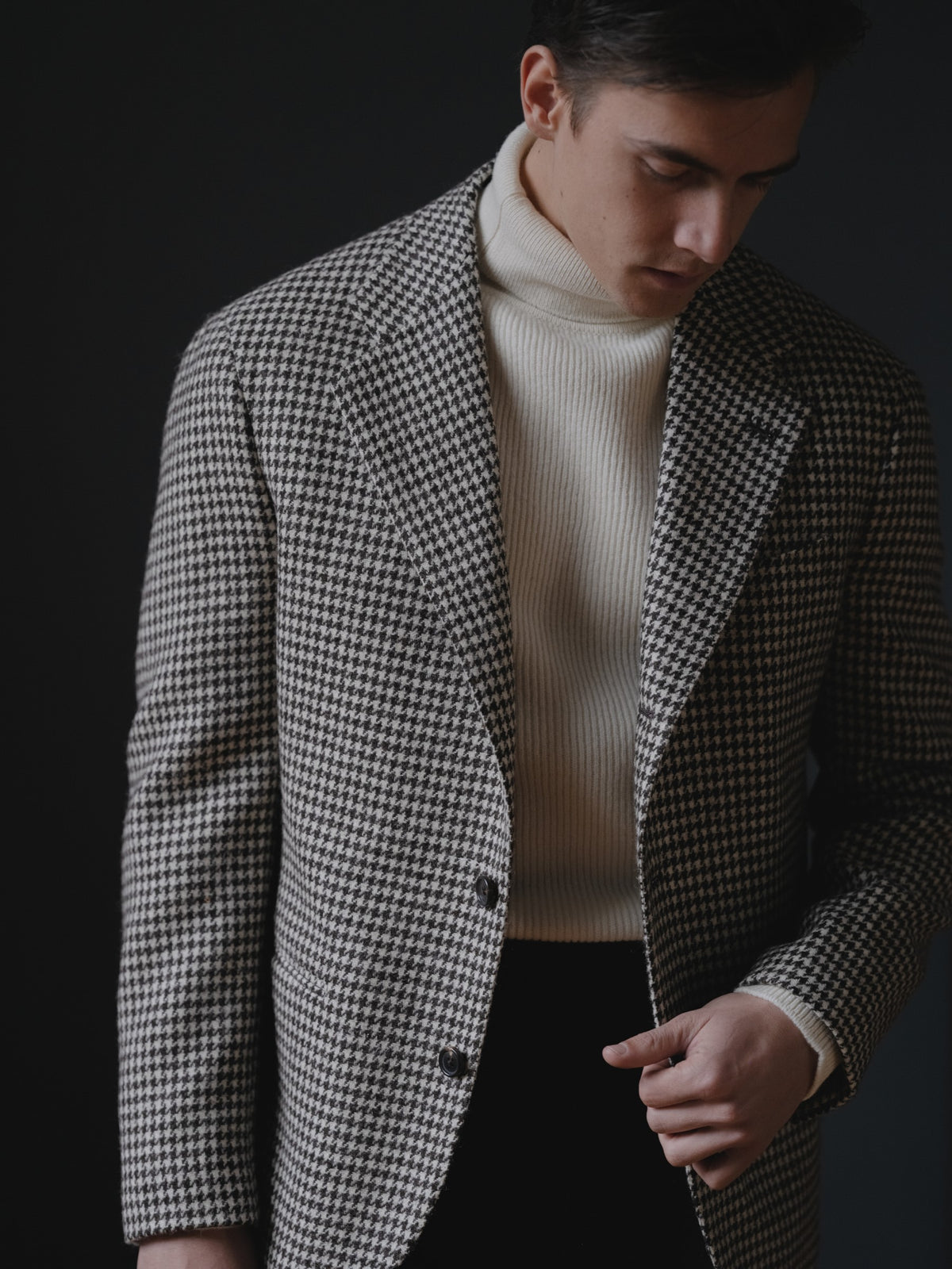 Man wearing a black white tweed houndstooth sport coat, charcoal flannel trousers and an ecru lambswool rollneck sweater