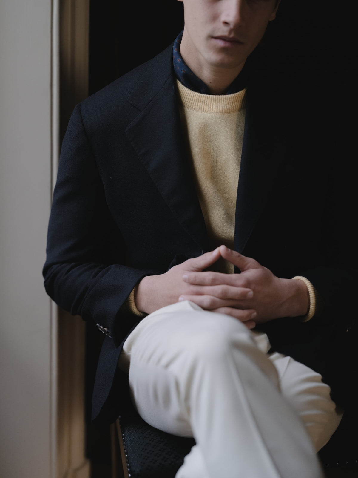 Man wearing a navy wool cashmere sport coat, a yellow crewneck sweater, cream flannels and a ancient madder neckerchief