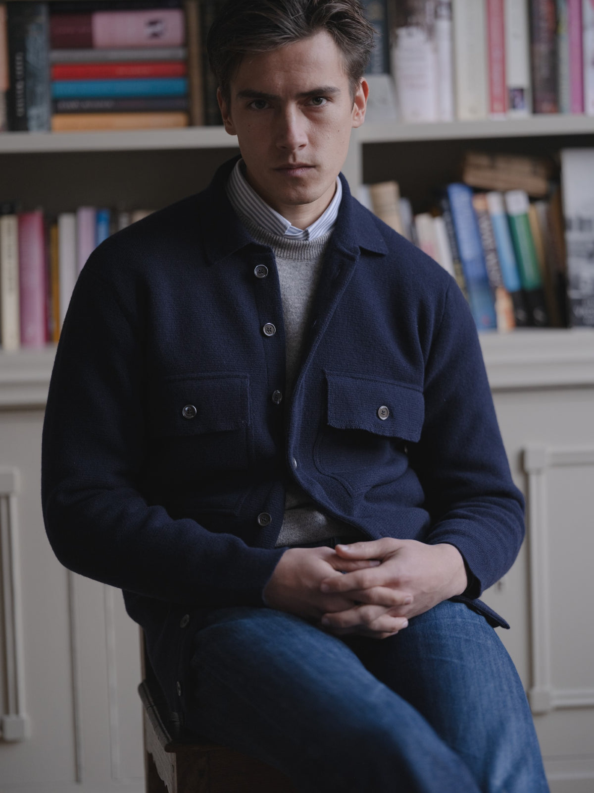 Man wearing a navy two pocket overshirt, stone washed jeans, grey crewneck and university stripe ocbd shirt