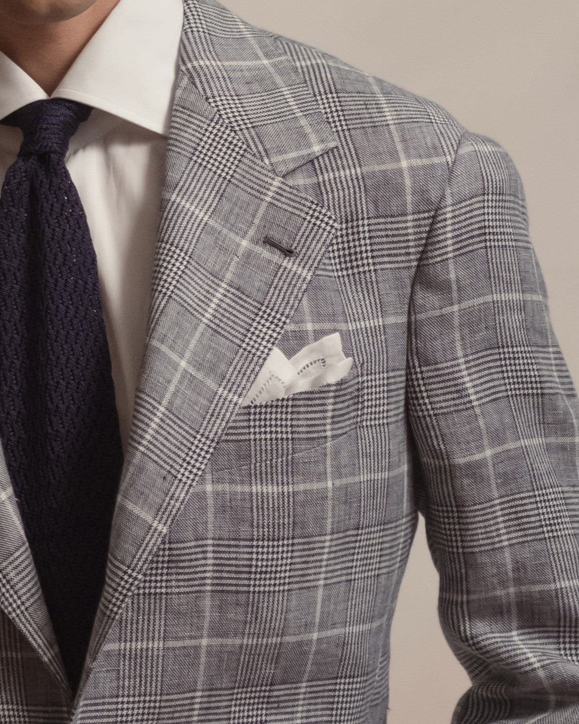 Man wearing navy glen check linen suit, white spread collar shirt, navy knitted zigzag tie and white linen pocket square with punched hem