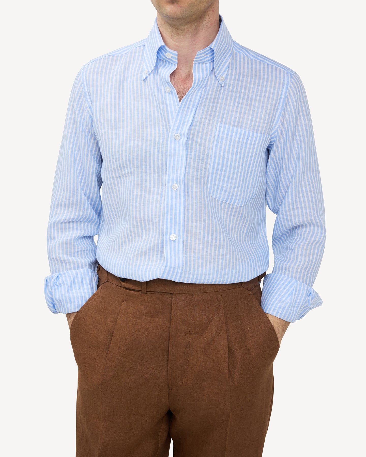 Man wearing light blue reverse stripe linen shirt and dark tan linen trousers