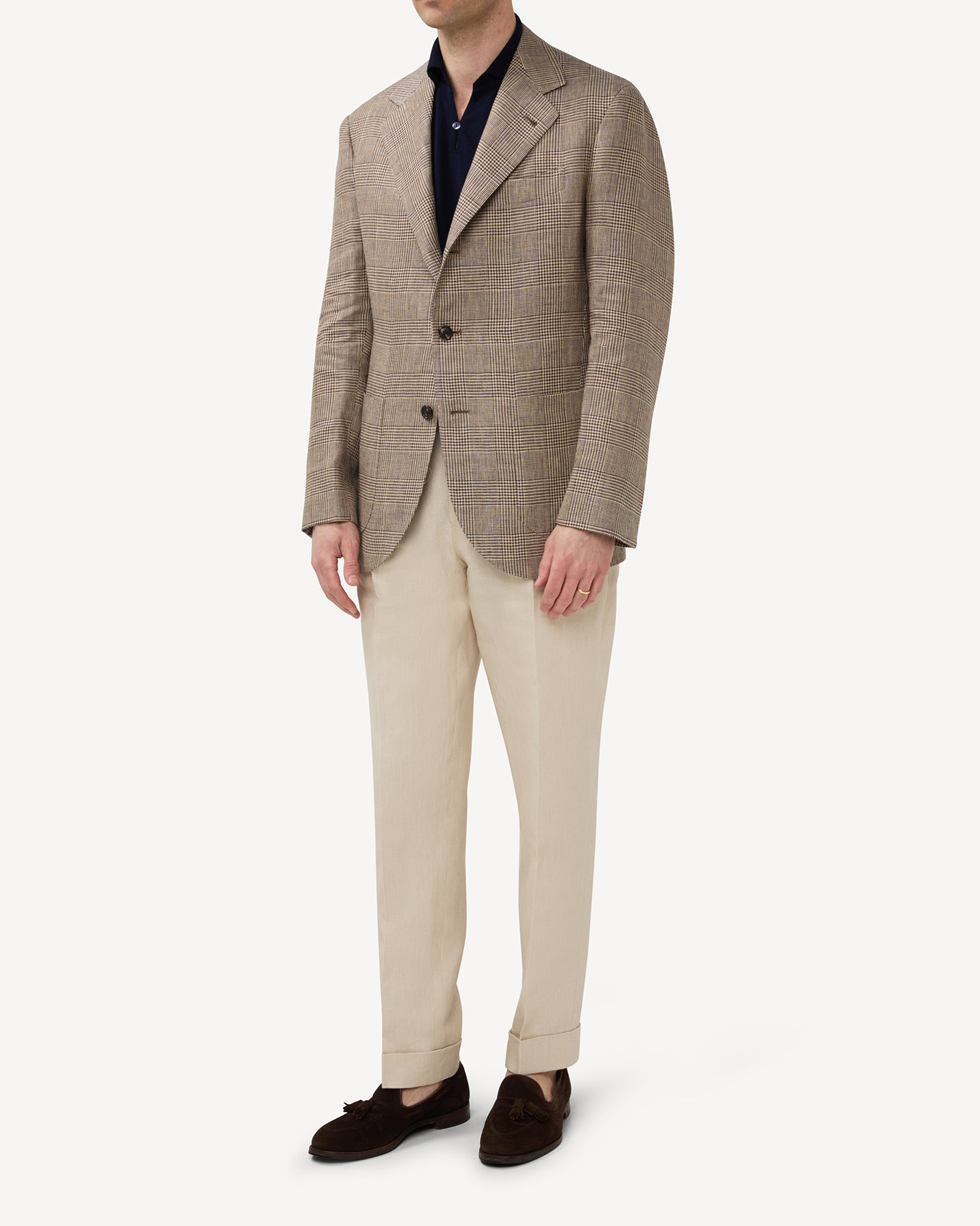 Man wearing a brown linen Prince of Wales sport coat, a navy skipper polo and stone coloured linen trousers