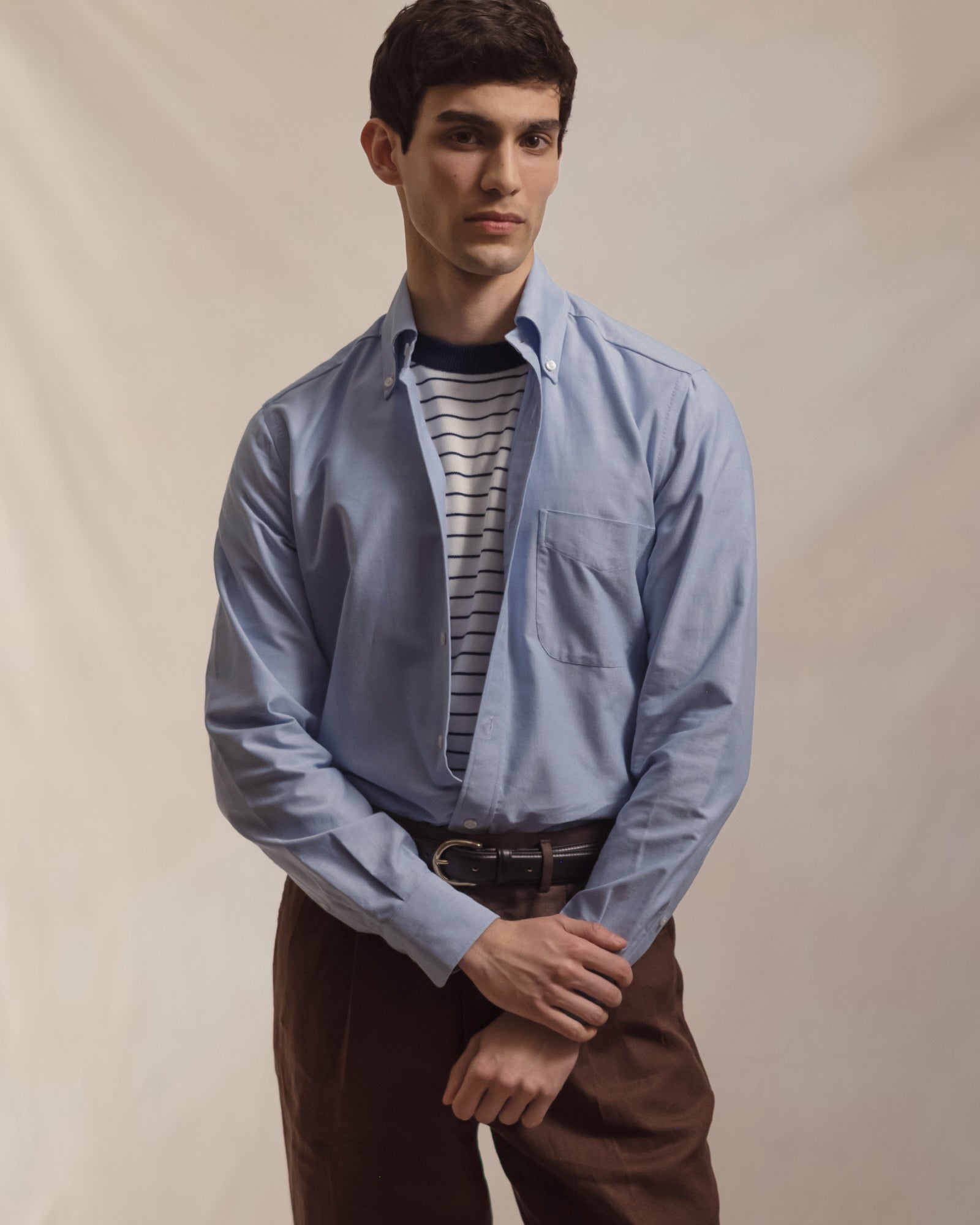 Man wearing a light blue OCBD, striped knitted t-shirt and brown linen trousers