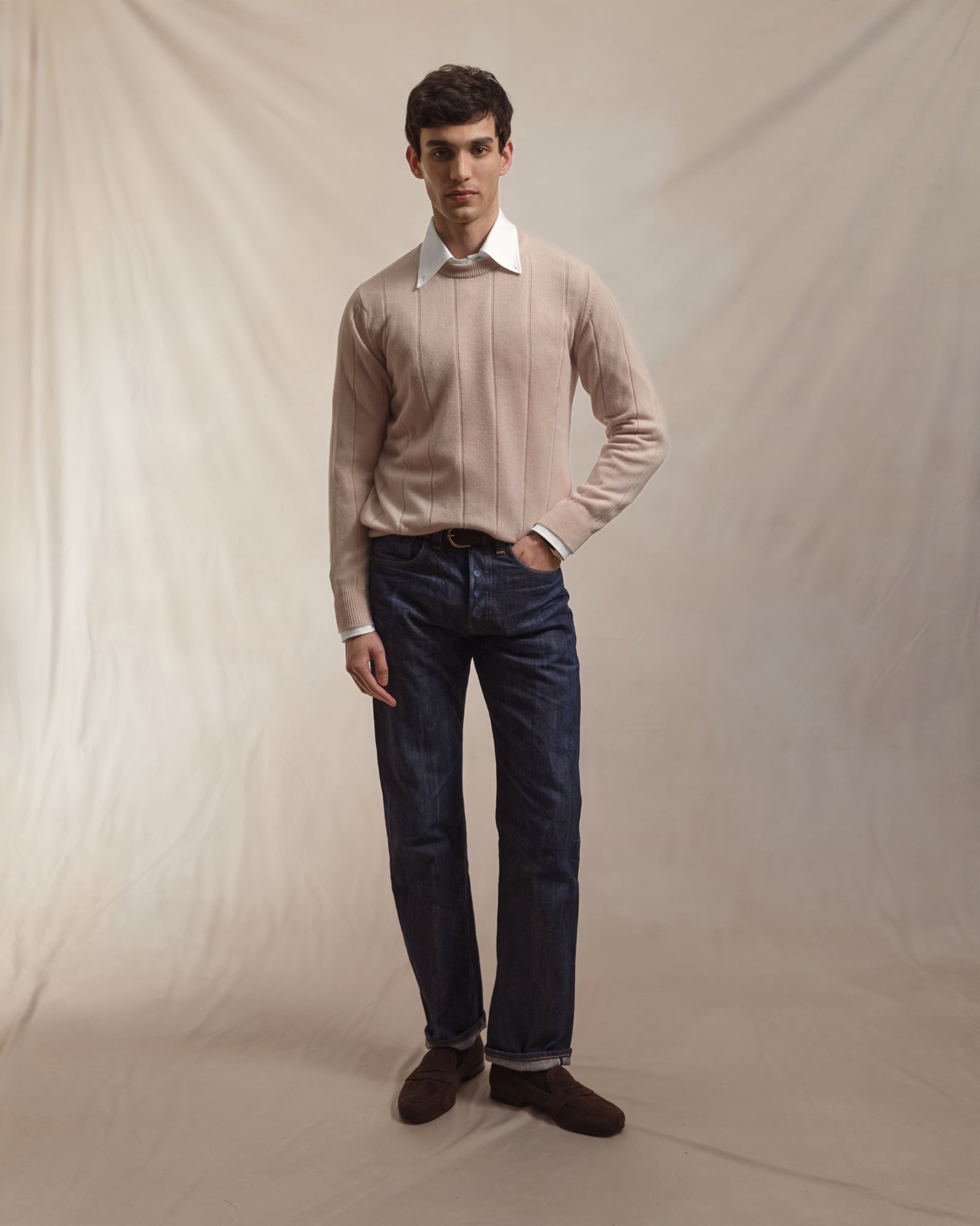 Man wearing a white OCBD shirt, ecru wide rib crew neck sweater and raw selvedge denim jeans