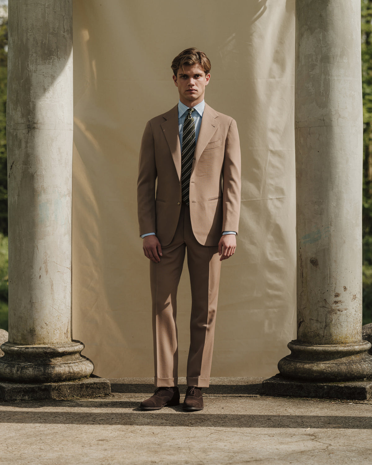 Man wearing tan gabardine suit, blue reverse stripe cotton linen shirt, green regimental stripe repp tie and brown suede oxford shoes