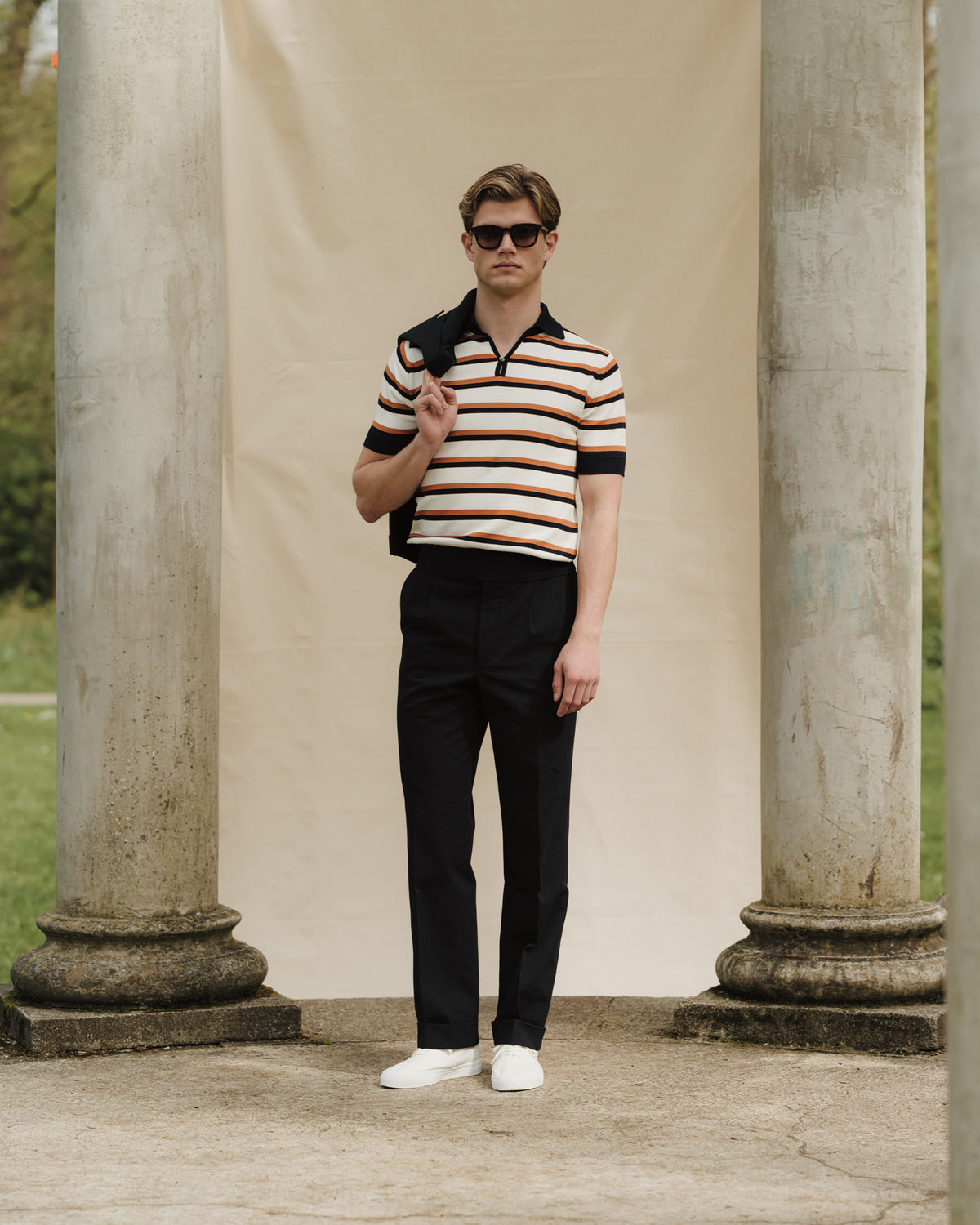 Man wearing navy seersucker suit, striped cotton skipper polo and white tennis sneakers