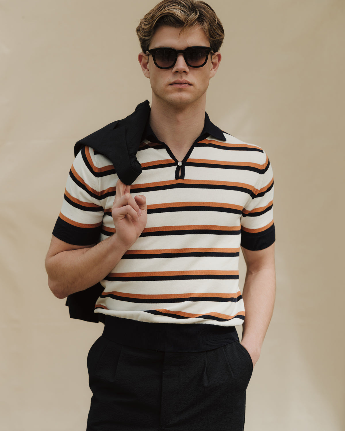 Man wearing navy trousers, striped cotton skipper polo with sunglasses