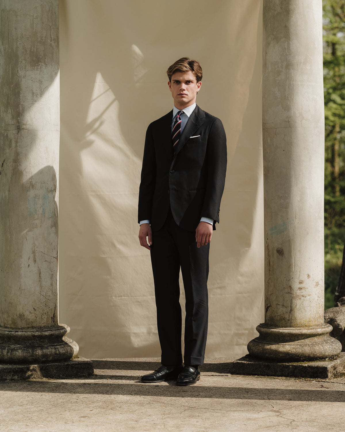 Man wearing navy hopsack suit, regimental stripe repp tie and black leather penny loafers