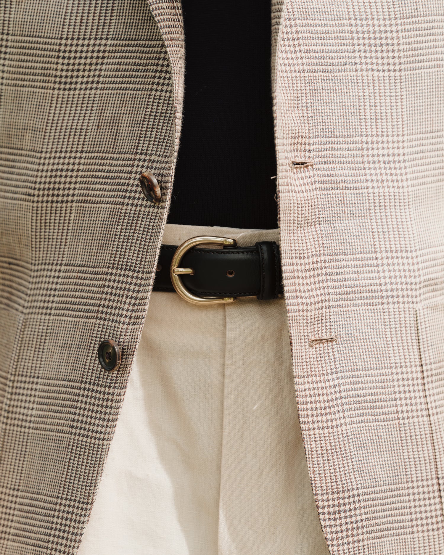 Man wearing stone linen trousers, black leather dress belt and beige brown linen prince of wales jacket