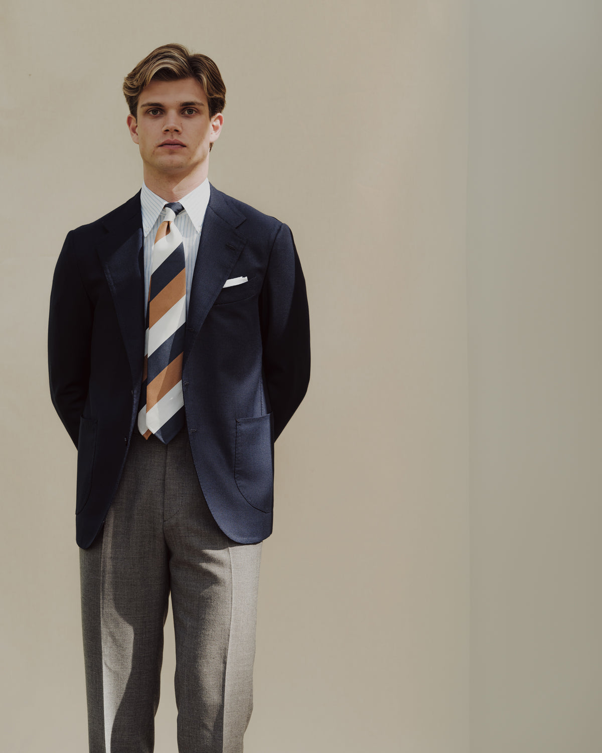 Man wearing light grey fresco trousers, dark blue sport coat and mogador block stripe tie