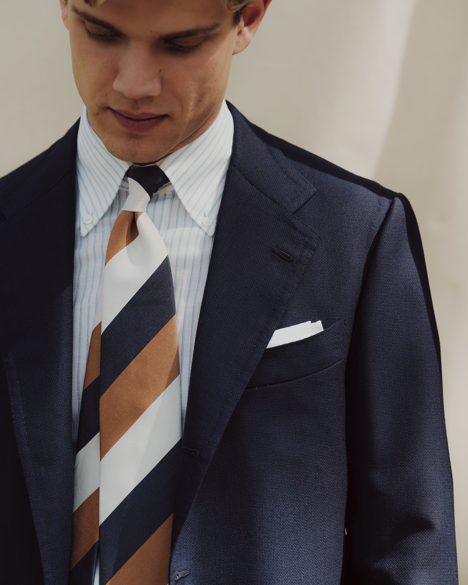 Man wearing a dark blue sport coat, cotton linen striped button down shirt and mogador block stripe tie
