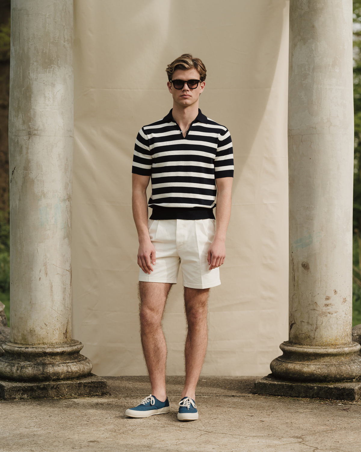 Man wearing a white navy striped skipper polo, white shorts and dark blue canvas sneakers