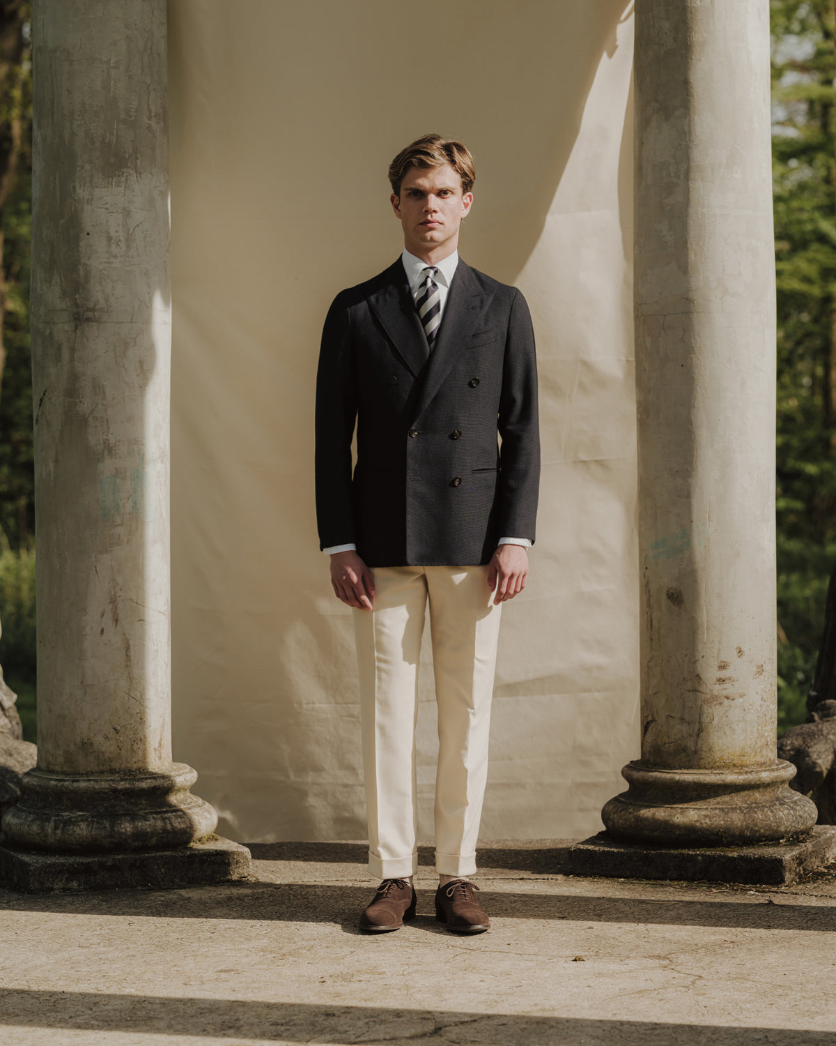 Man wearing navy double breasted blazer, cream Fox Brothers cricket flannel trousers and navy white repp tie