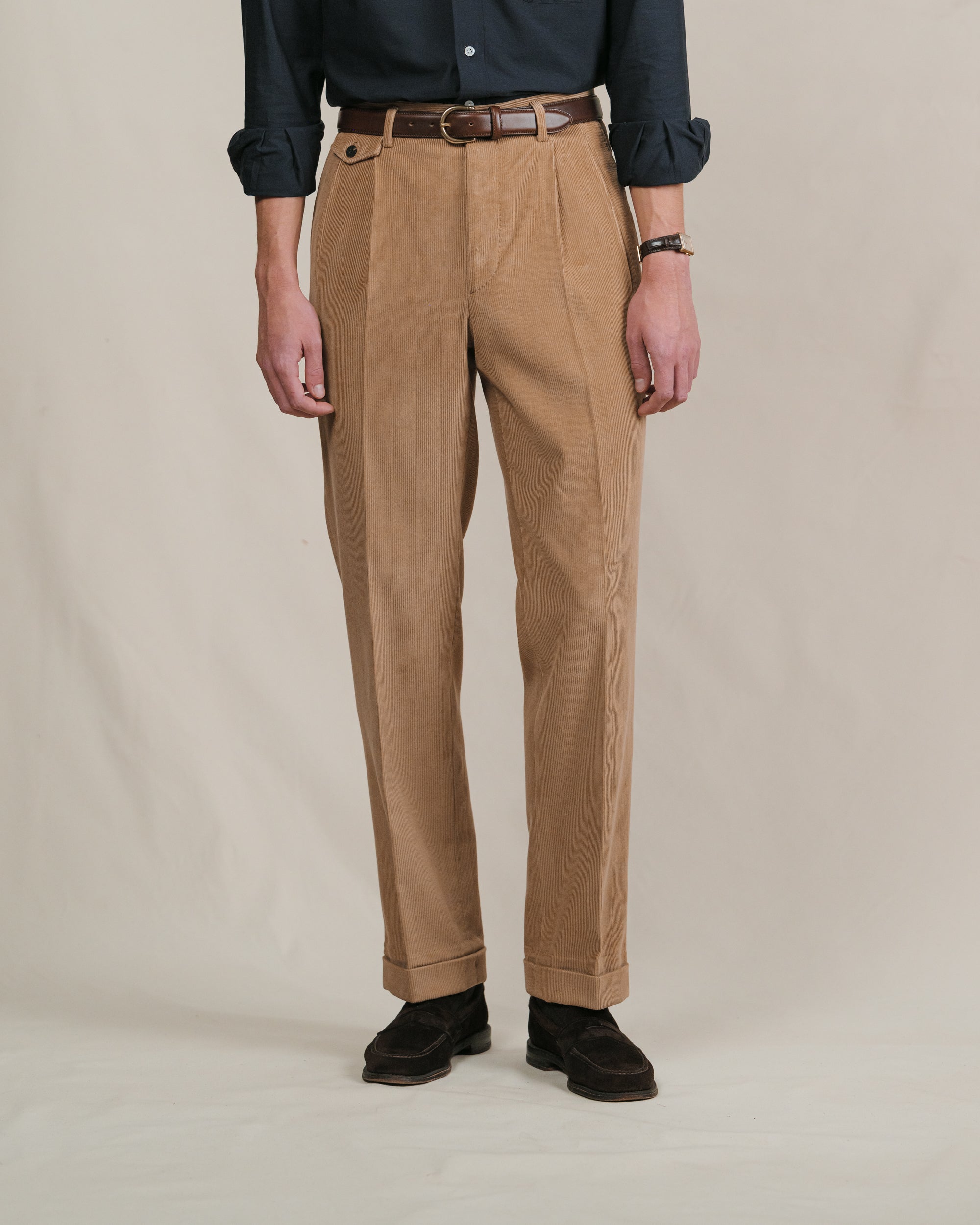 Person wearing brown corduroy trousers, navy shirt, brown leather belt and suede penny loafers