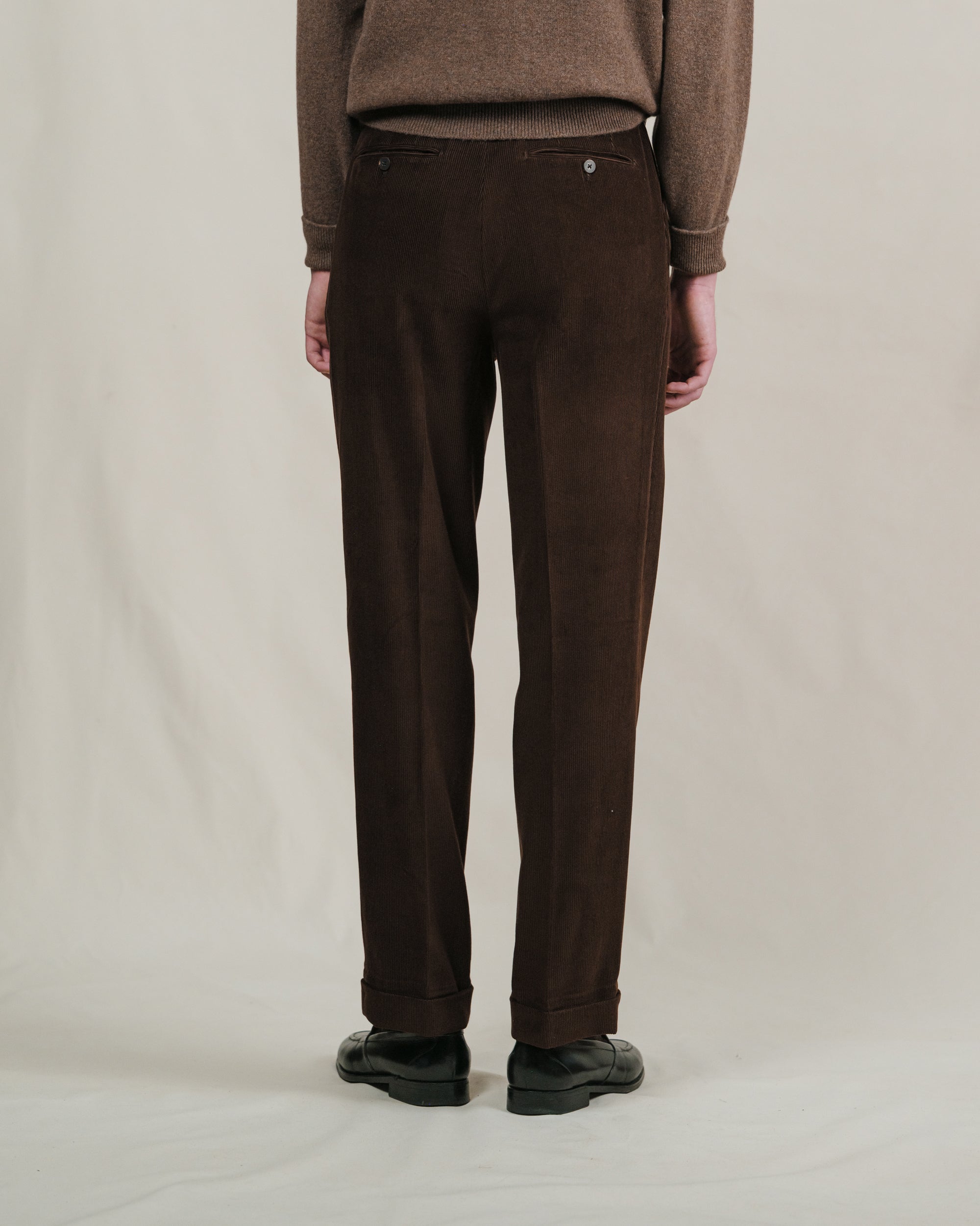Person wearing brown corduroy pants and a matching sweater on a plain background