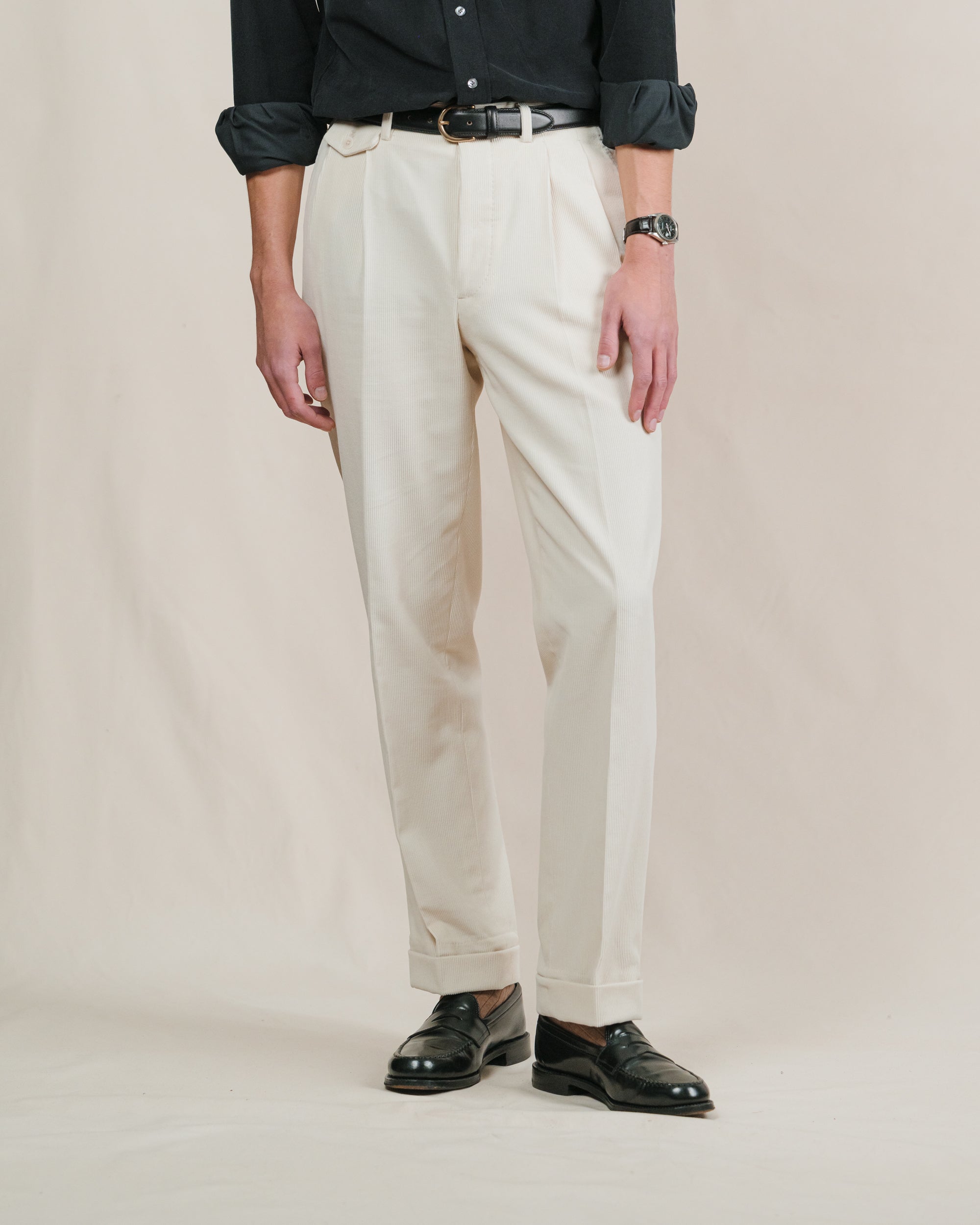 Person wearing cream corduroy pants and black shoes on a plain background