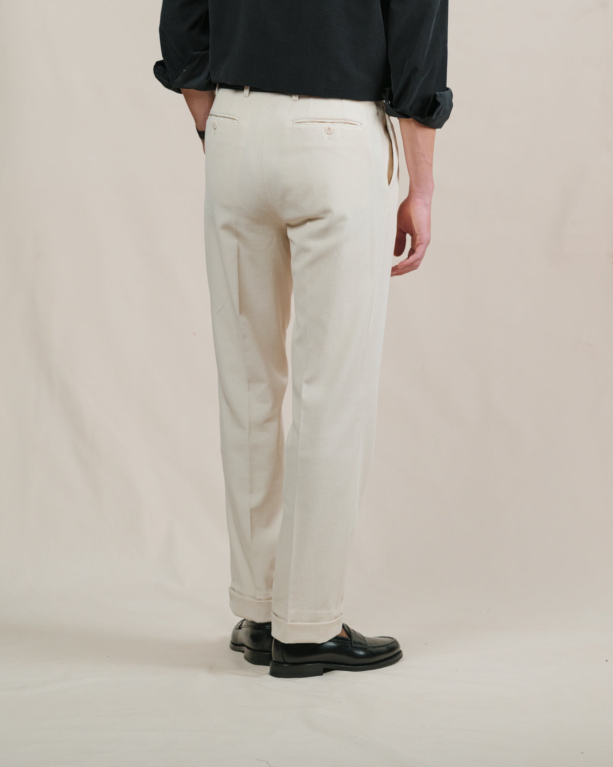 Person wearing cream corduroy pants and black shoes on a plain background