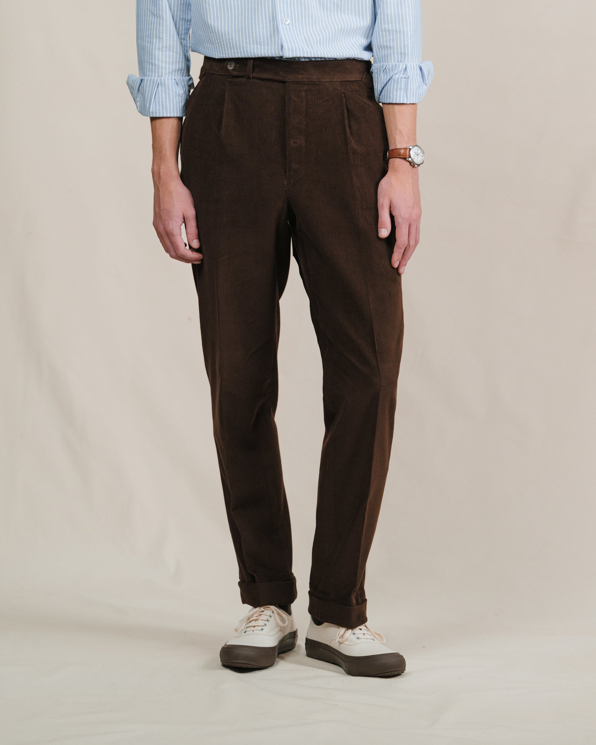 Person wearing brown corduroy pants, a light blue shirt and ecru tennis sneakers with brown sole