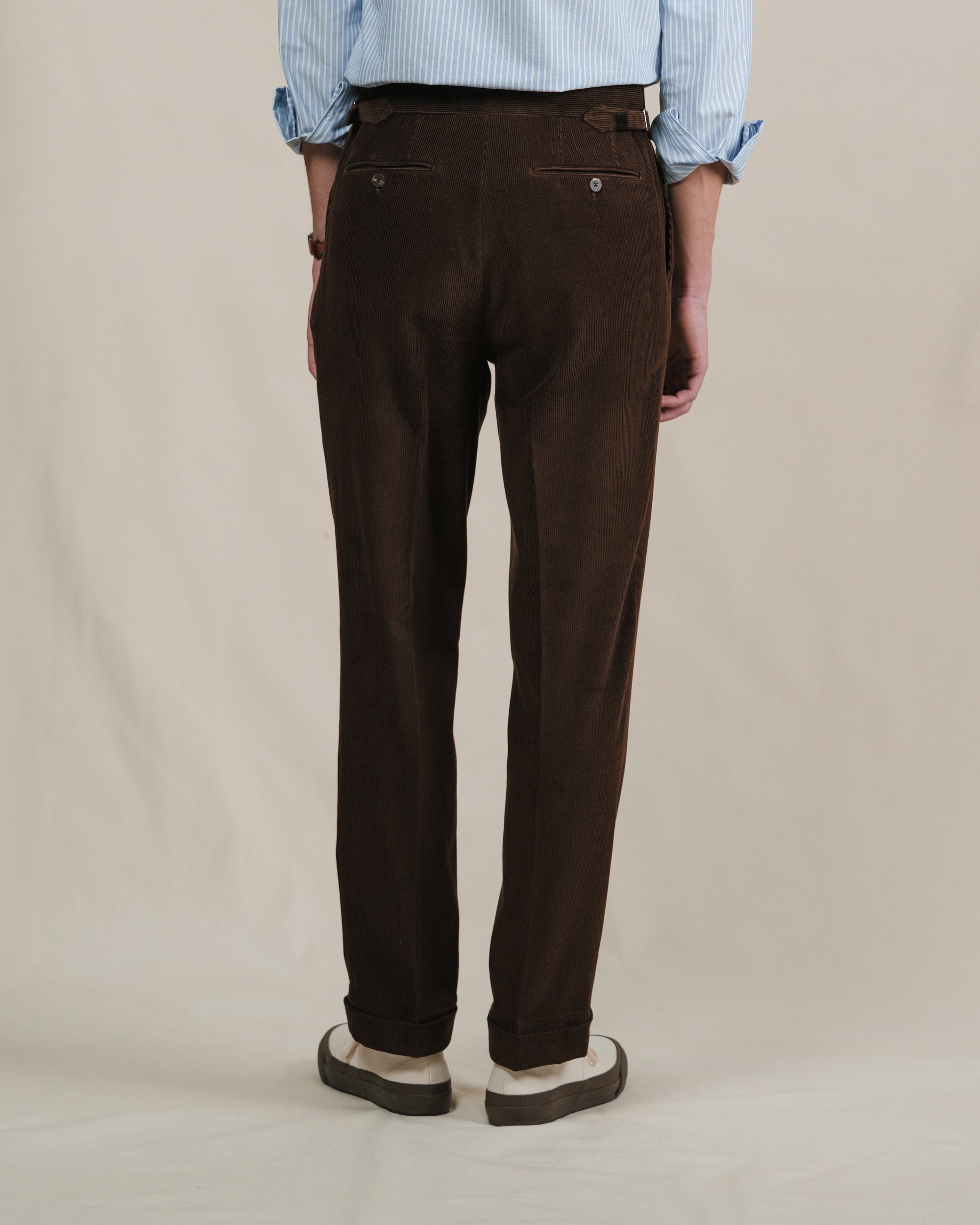 Brown corduroy pants worn by a person on a beige background