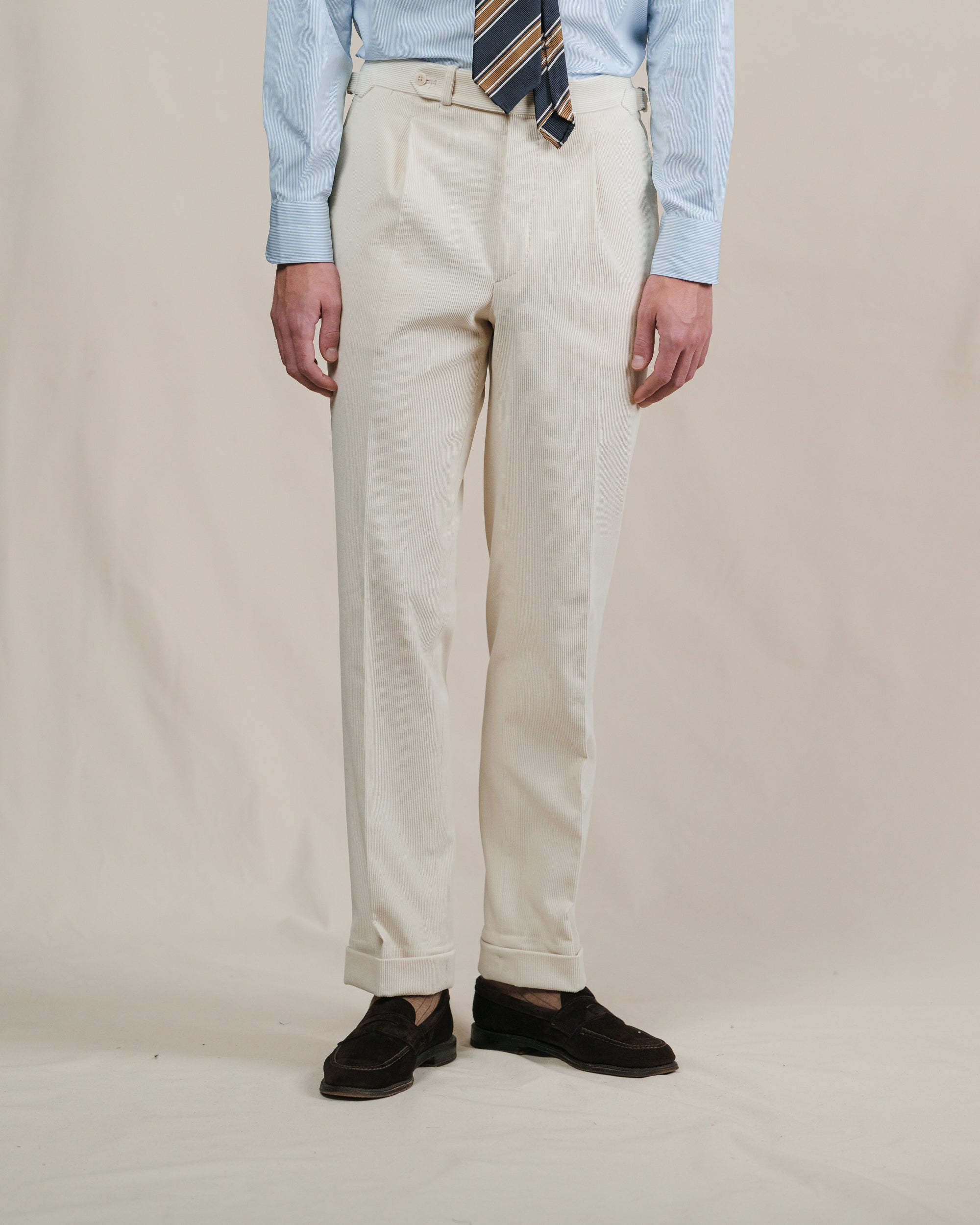 Person wearing cream corduroy pants with a striped tie and light blue shirt on a plain background