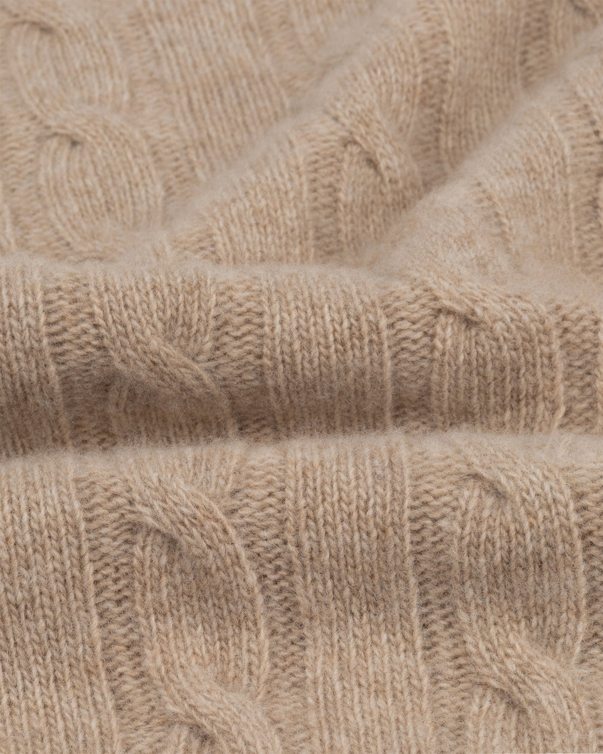 Close-up van de zachte kabelstructuur van een beige trui van merinowol en kasjmier