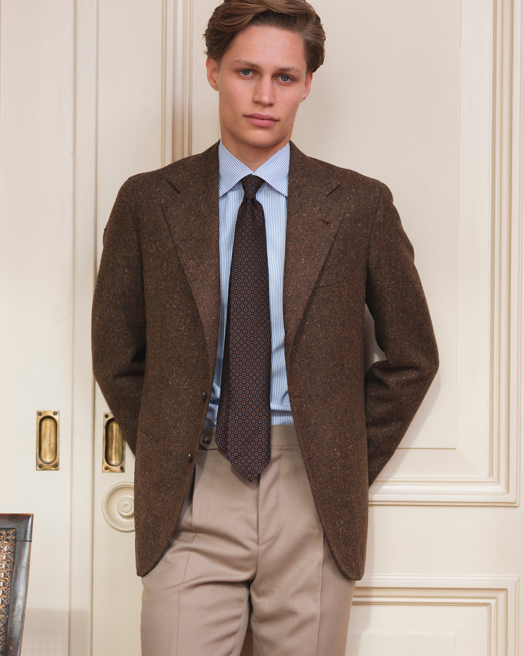 Man wearing a brown Donegal tweed sport coat, beige cavalry twill trousers, bengal stripe shirt and a navy patterned ancient madder tie