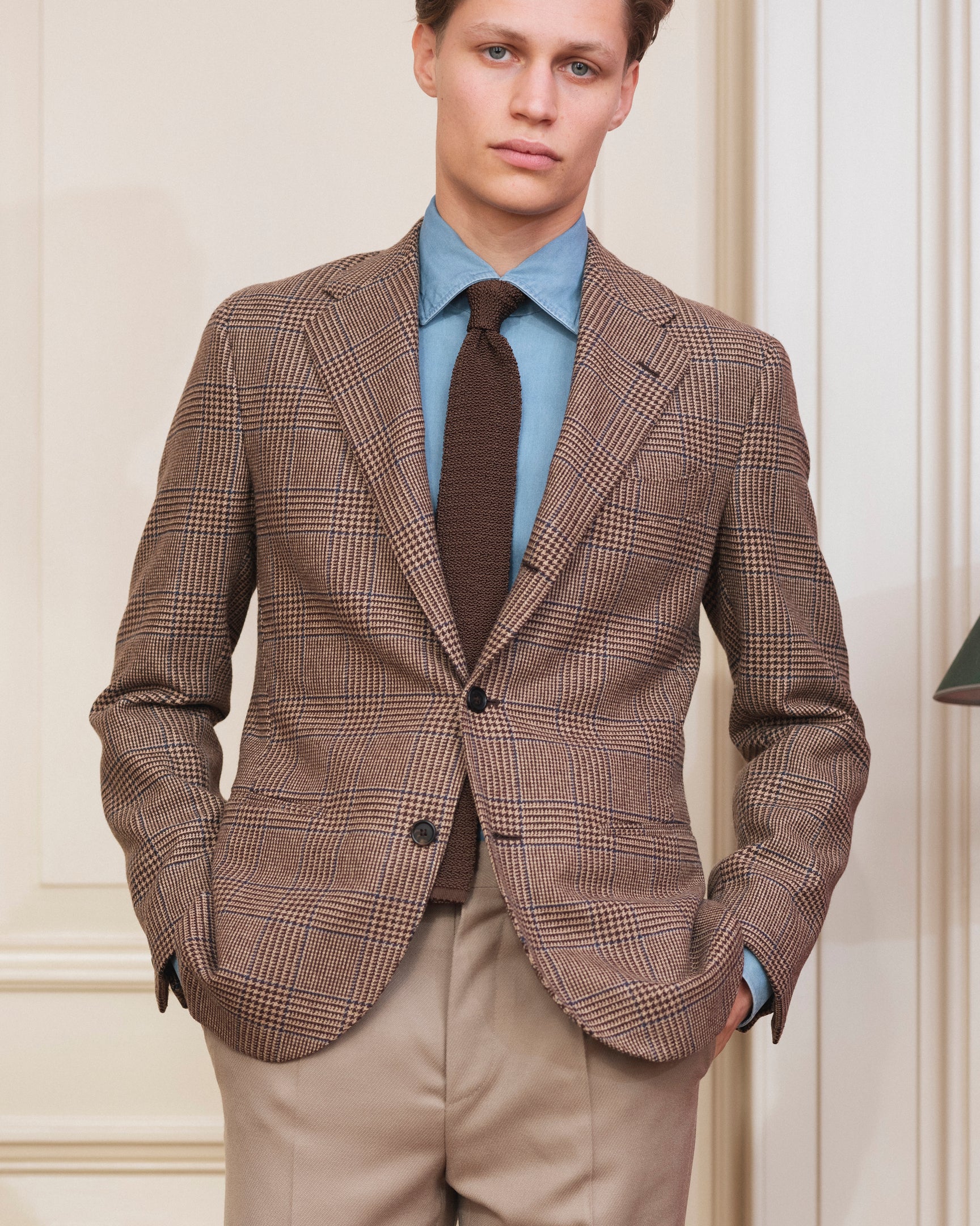 Man wearing a brown tweed prince of wales check sport coat, beige cavalry twill trousers, denim shirt and brown knitted silk tie