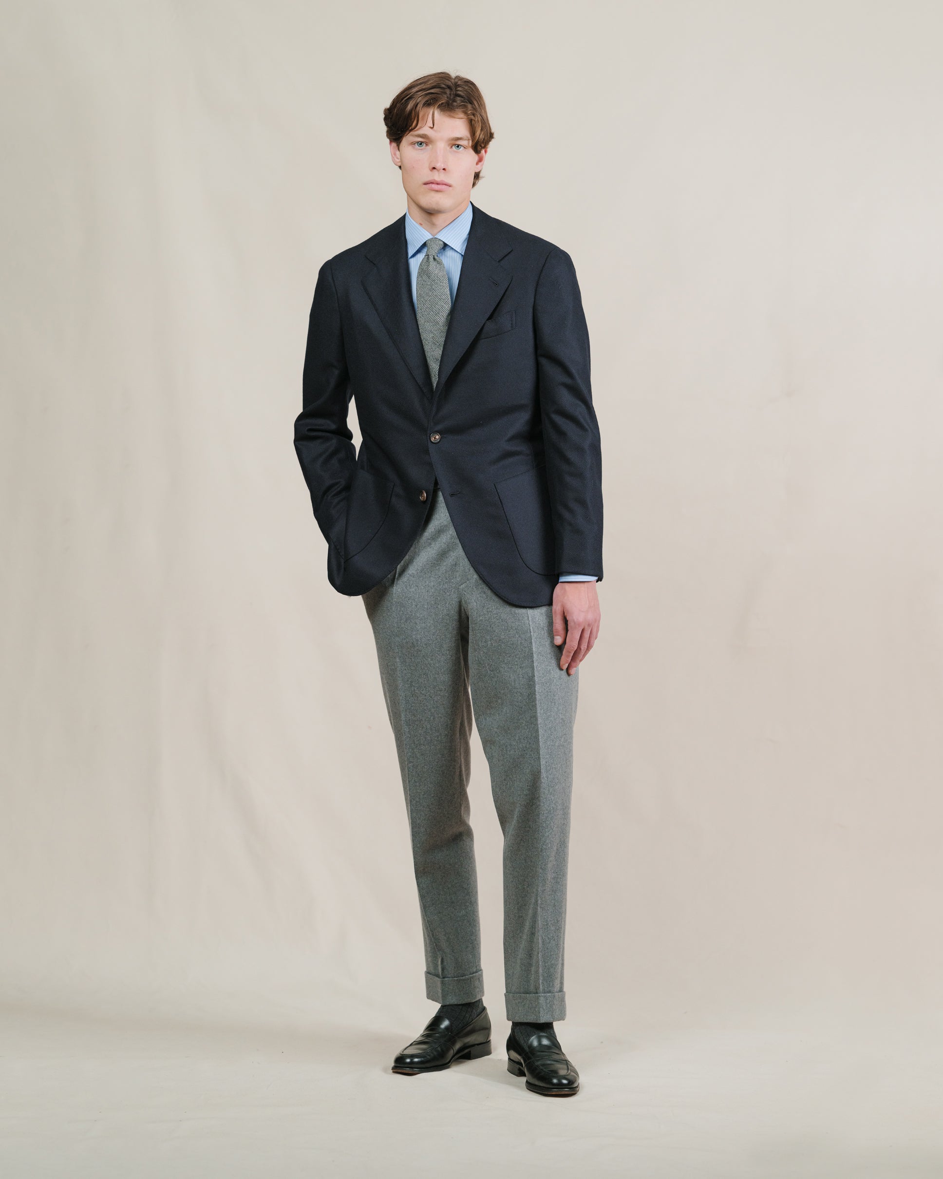 Man wearing a pair of light grey flannel trousers, light blue striped shirt, grey tie and navy sport coat