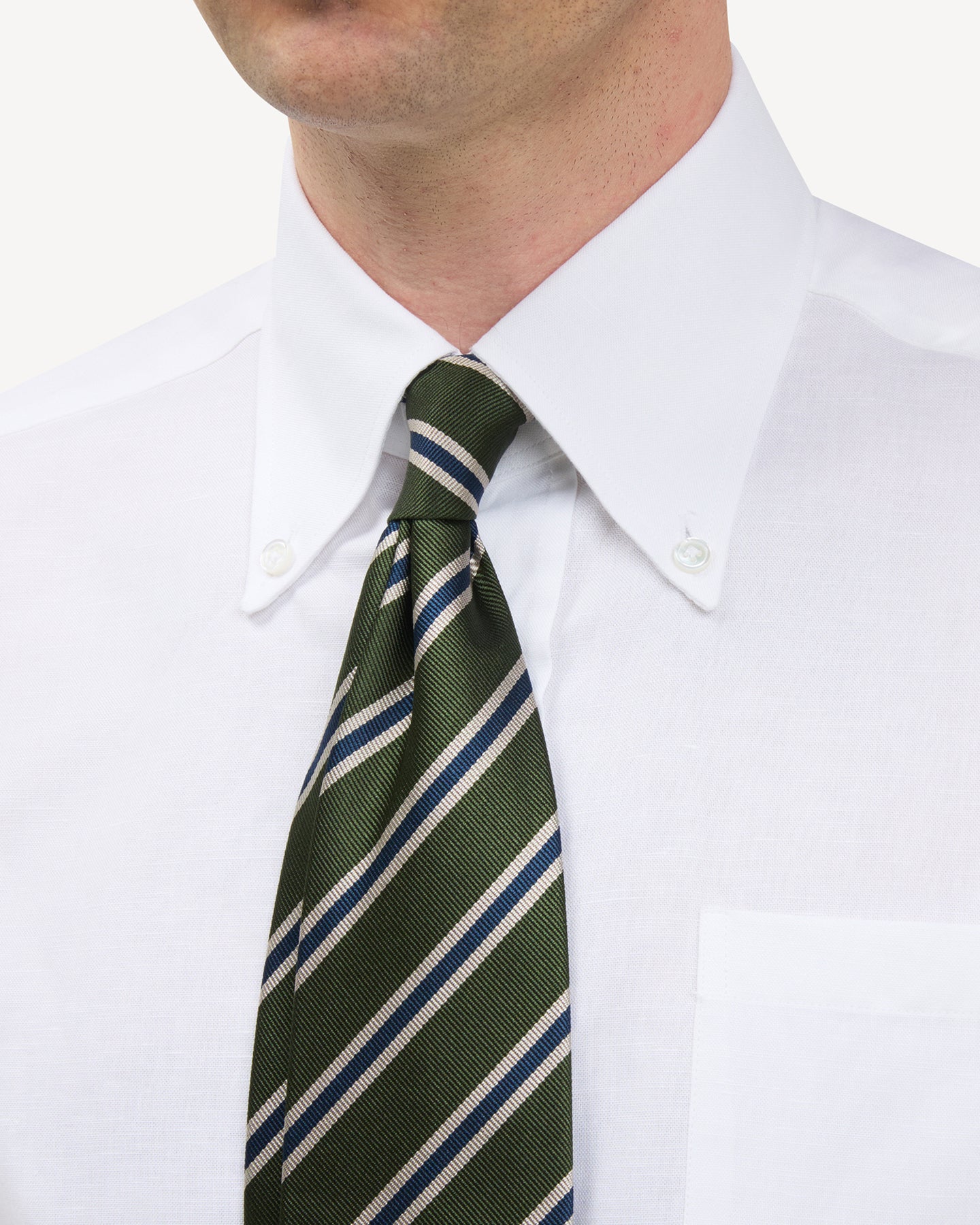 Man wearing a white button down shirt and a green, tan and navy regimental stripe repp tie