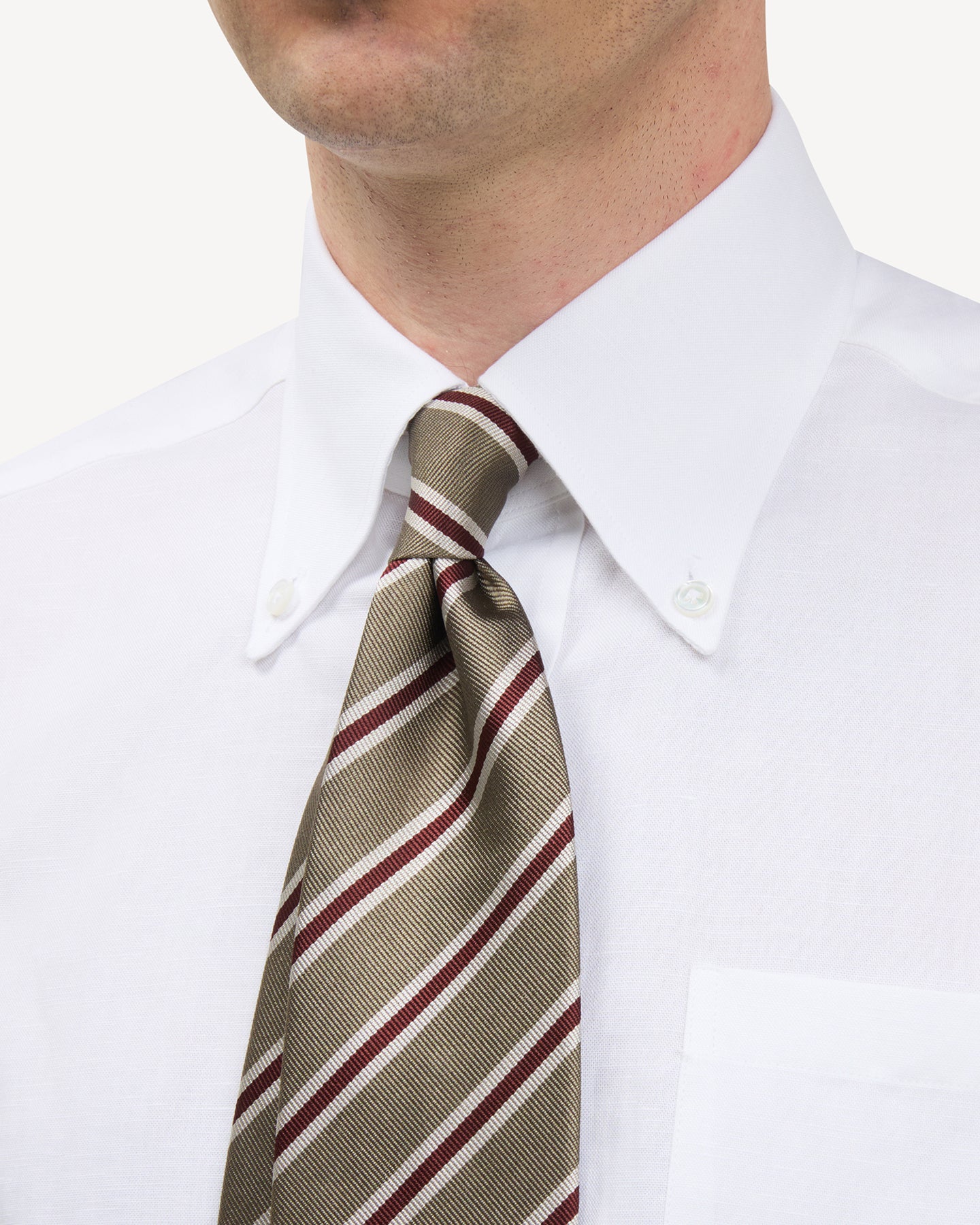 Man wearing a white button down shirt and light green, tan and red regimental stripe repp tie