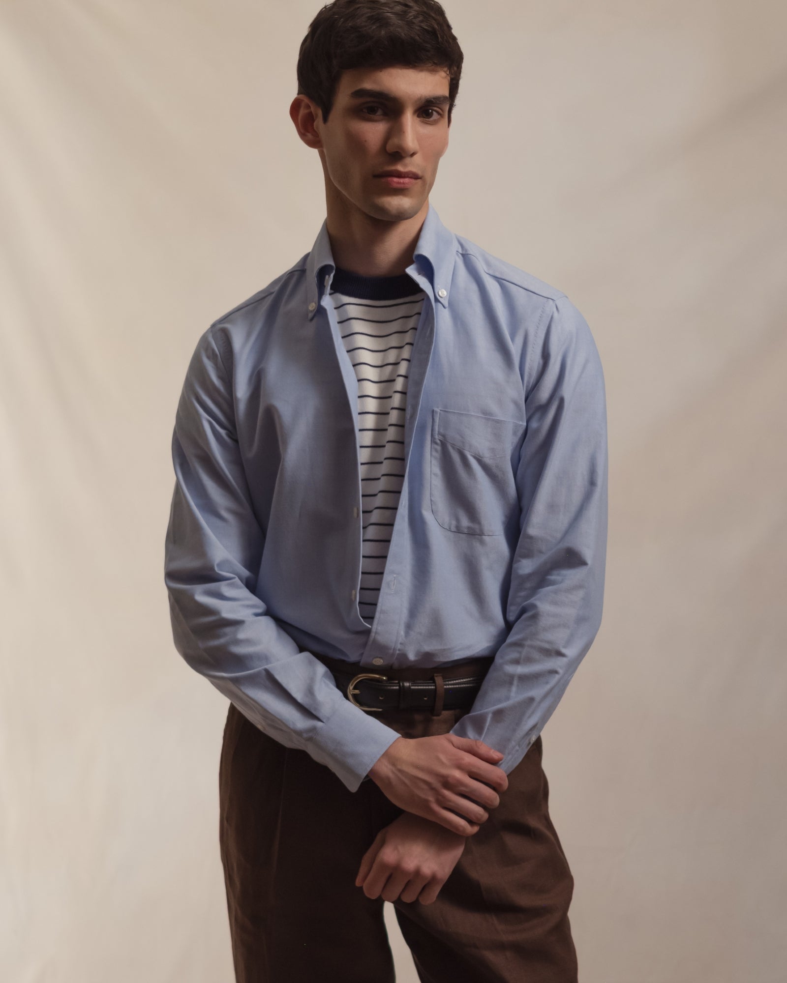 Man wearing a light blue OCBD, striped knitted t-shirt and brown linen trousers