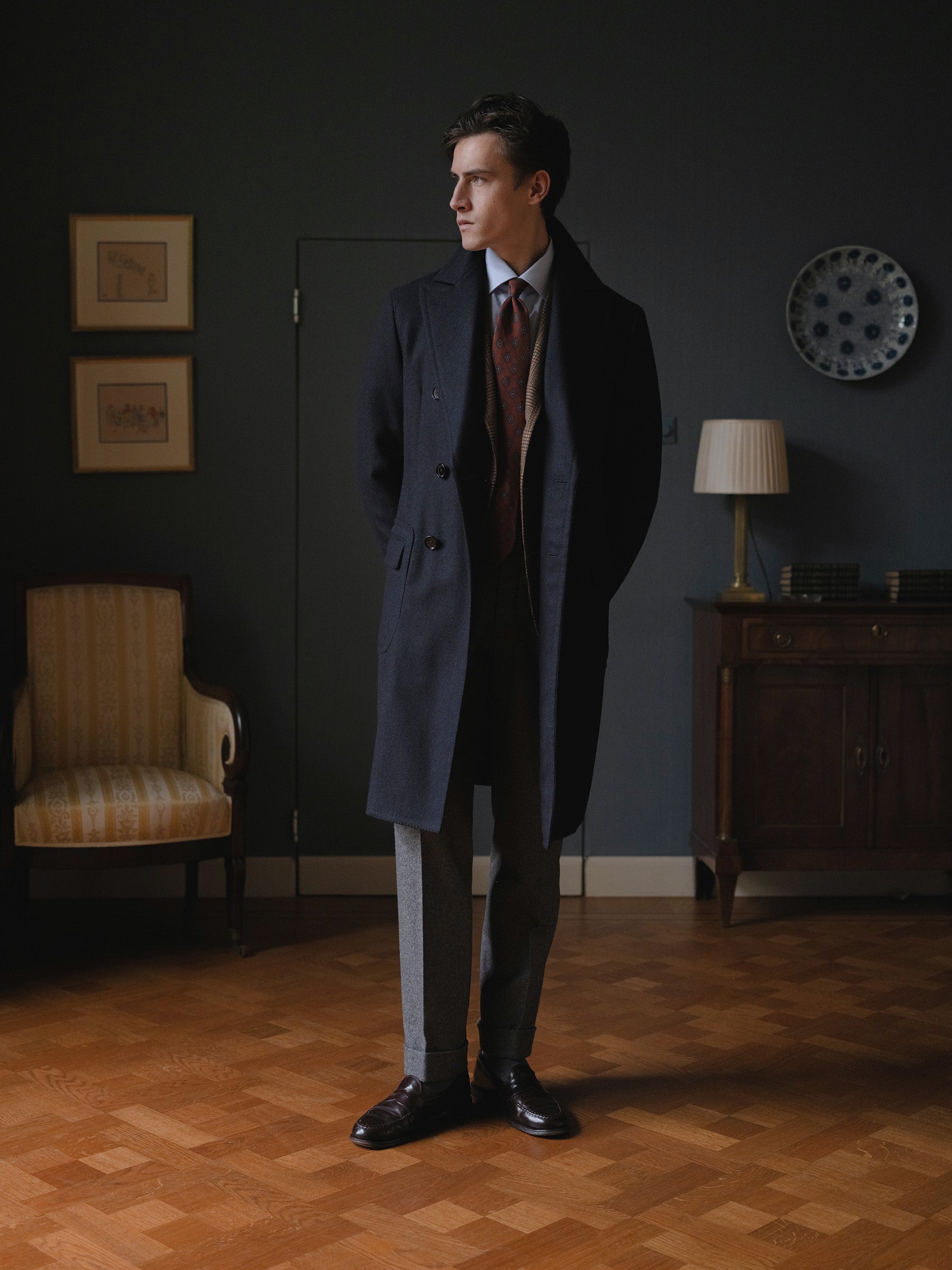 Man wearing a navy polo coat, brown prince of wales sport coat and mid grey flannel trousers