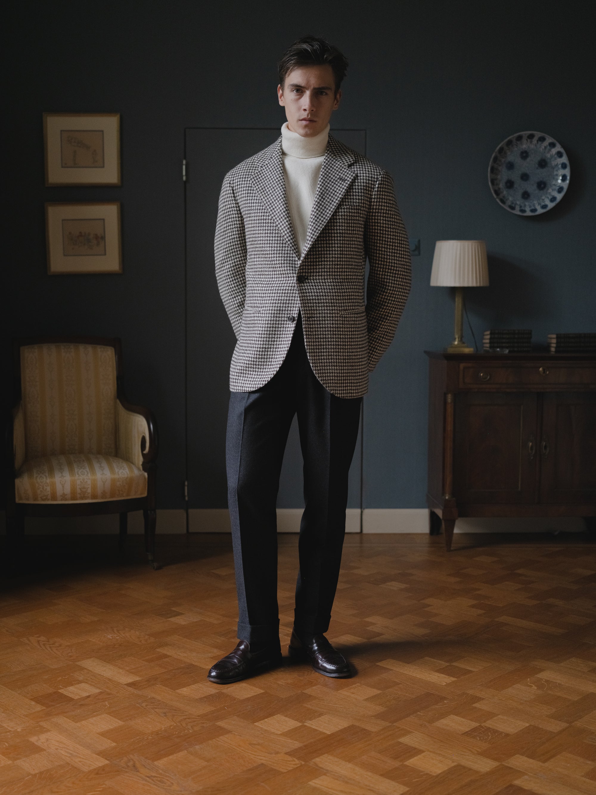 Man wearing a black white tweed houndstooth sport coat, charcoal flannel trousers and an ecru lambswool rollneck sweater