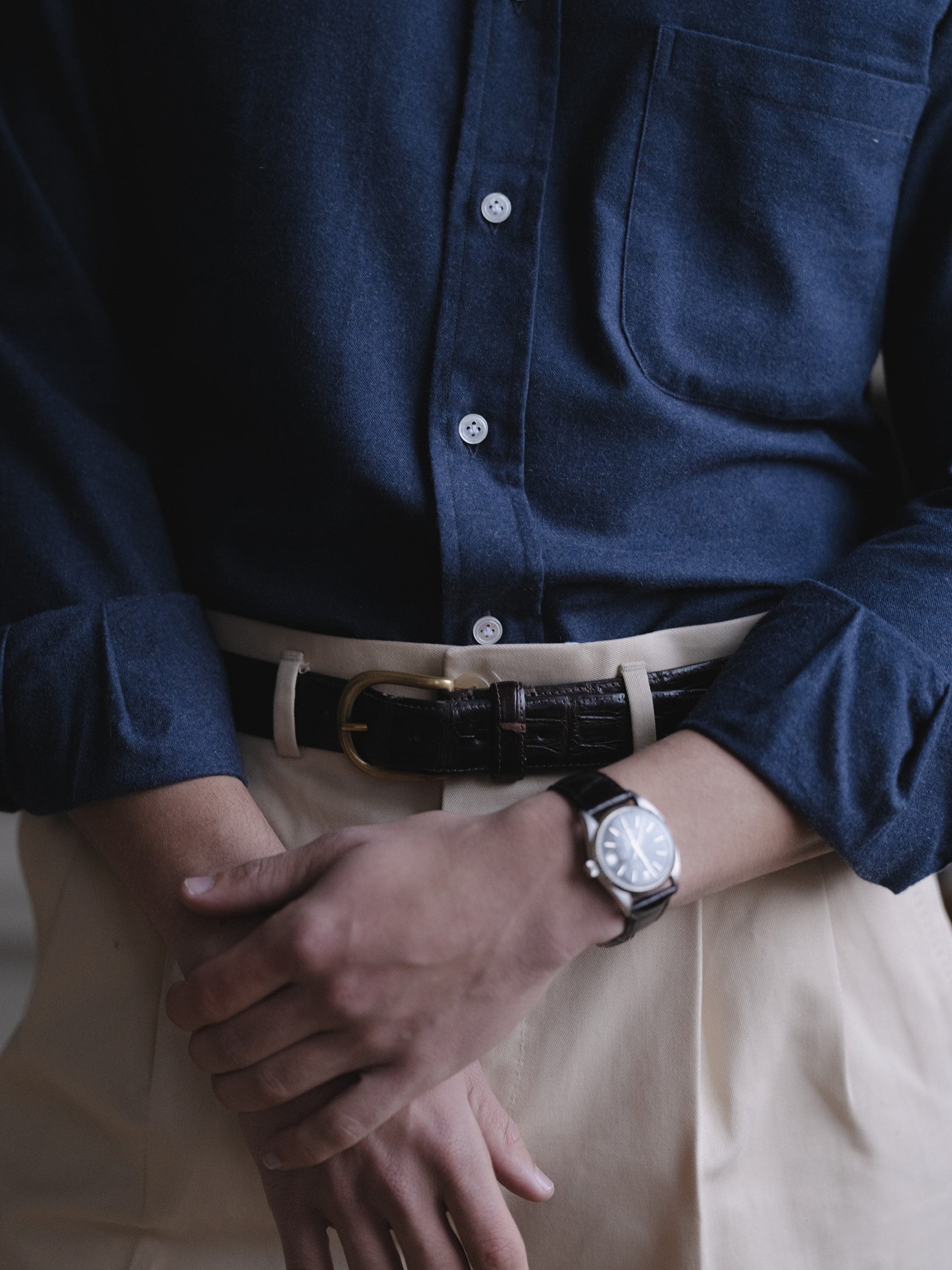 Man wearing a navy cotton cashmere button down shirt, cream cotton drill trousers and brown crocodile dress belt