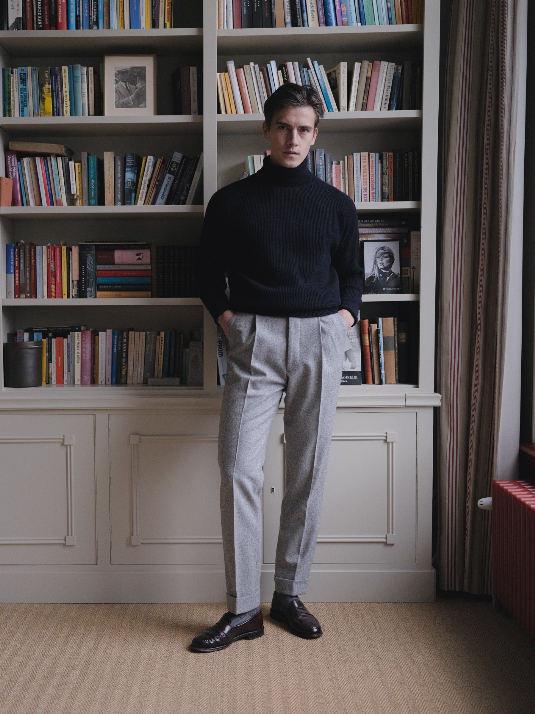 Man wearing a navy roll neck sweater and light grey flannel trousers