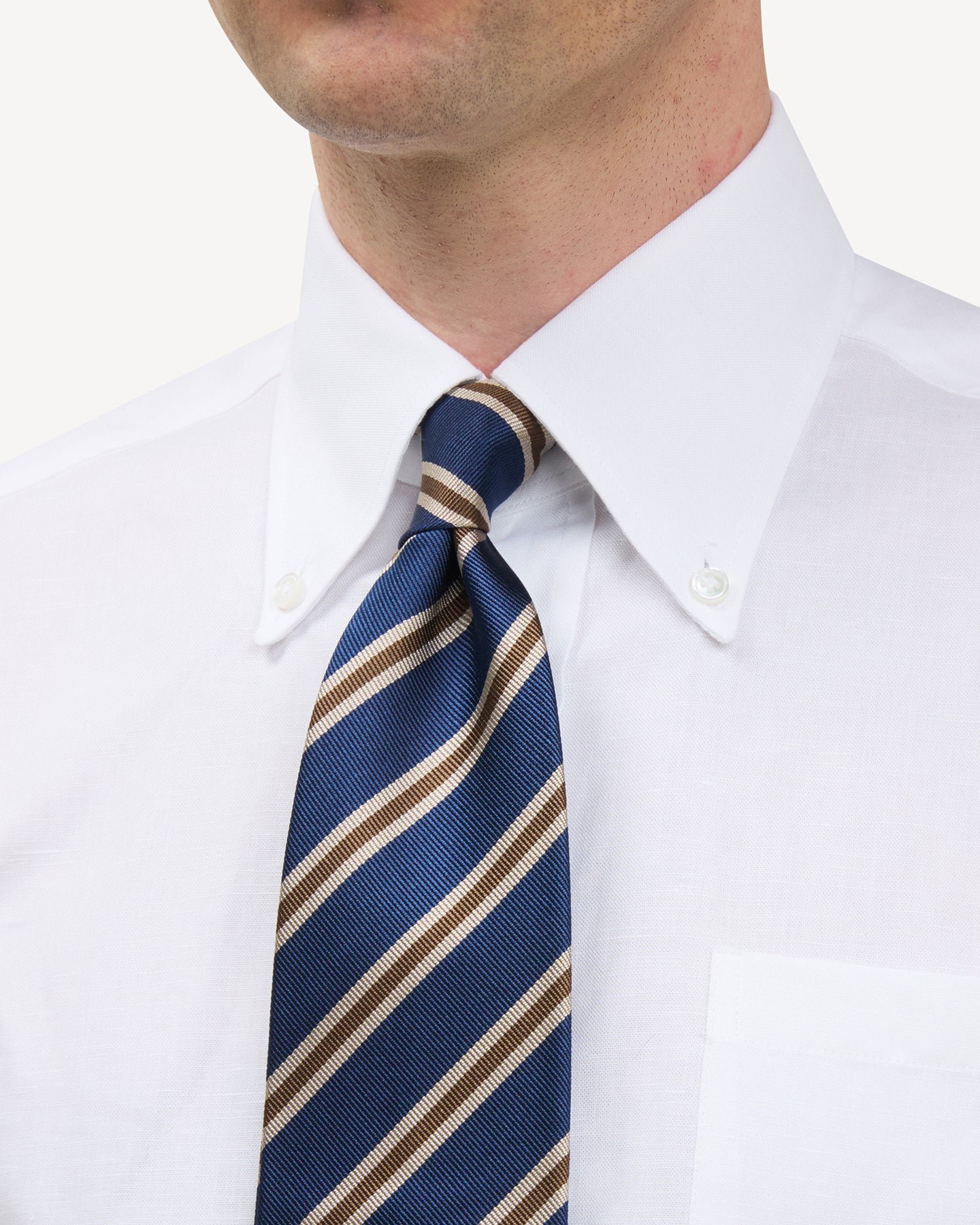 Man wearing a white button down shirt and a blue, tan and mid brown regimental stripe repp tie
