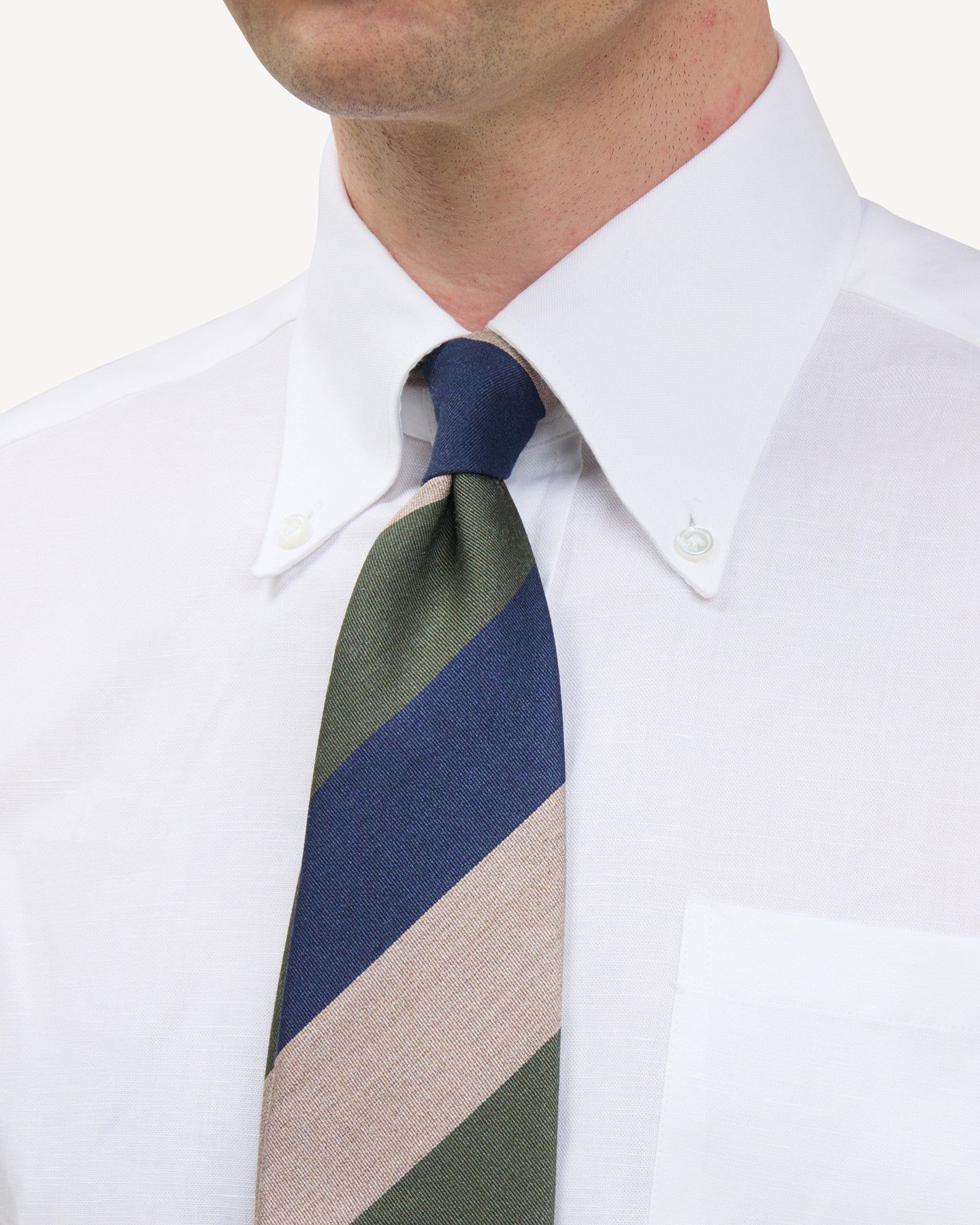 Man wearing a white button down shirt and a navy, beige and green block stripe mogador tie