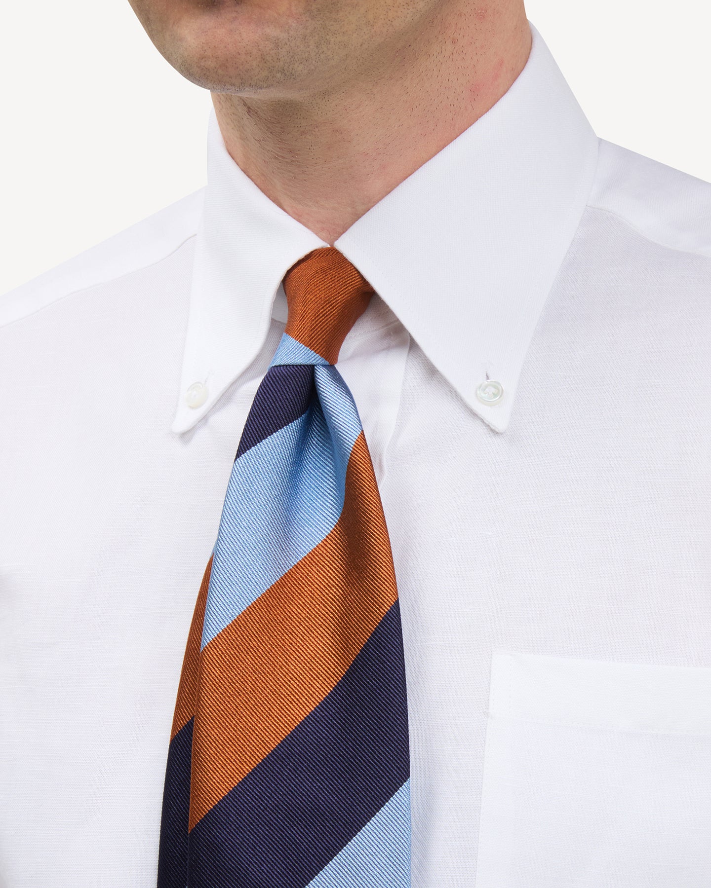 Man wearing a white button down shirt and navy, blue and orange block stripe repp tie