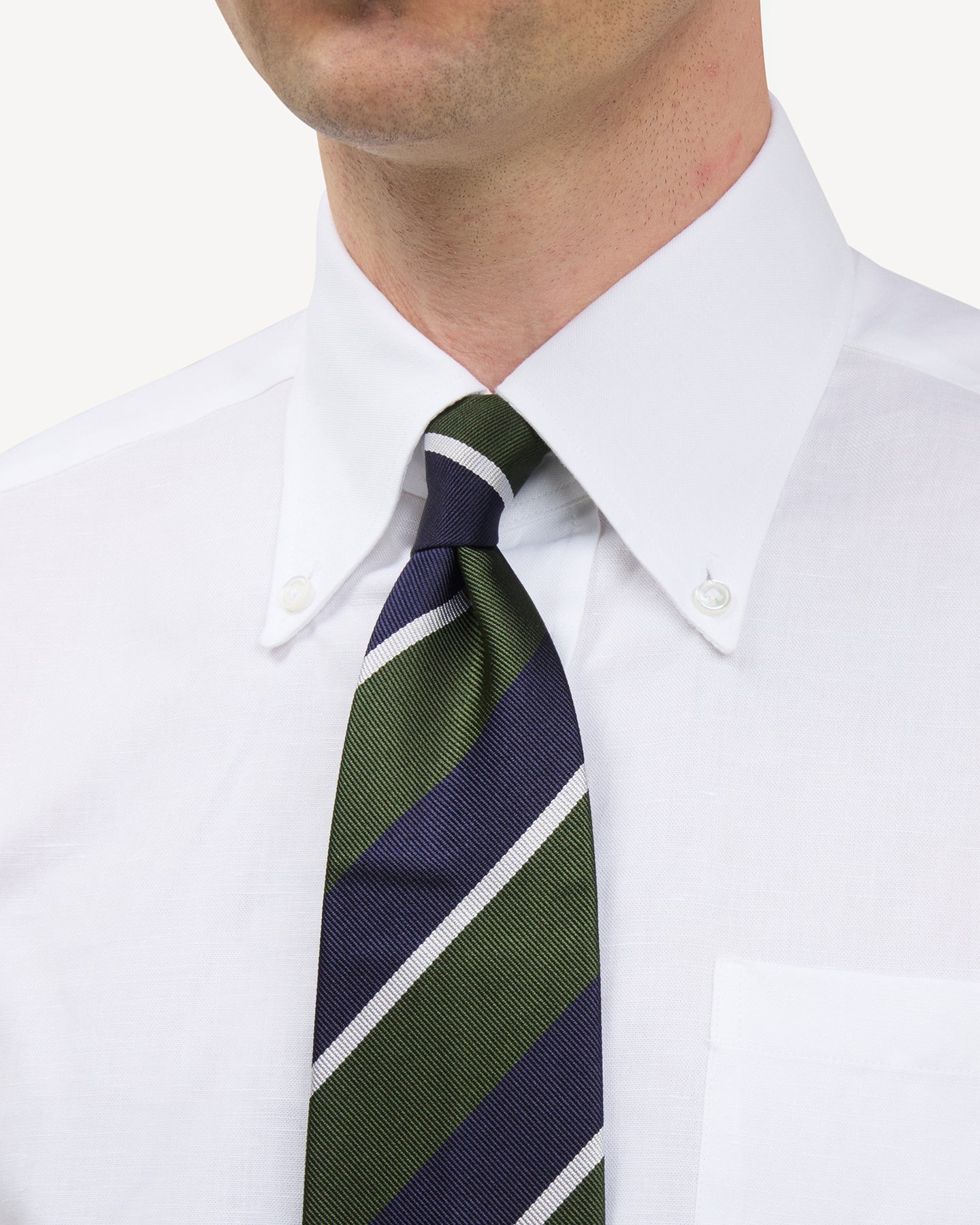 Man wearing a white button down shirt and a navy, green and white regimental stripe repp tie