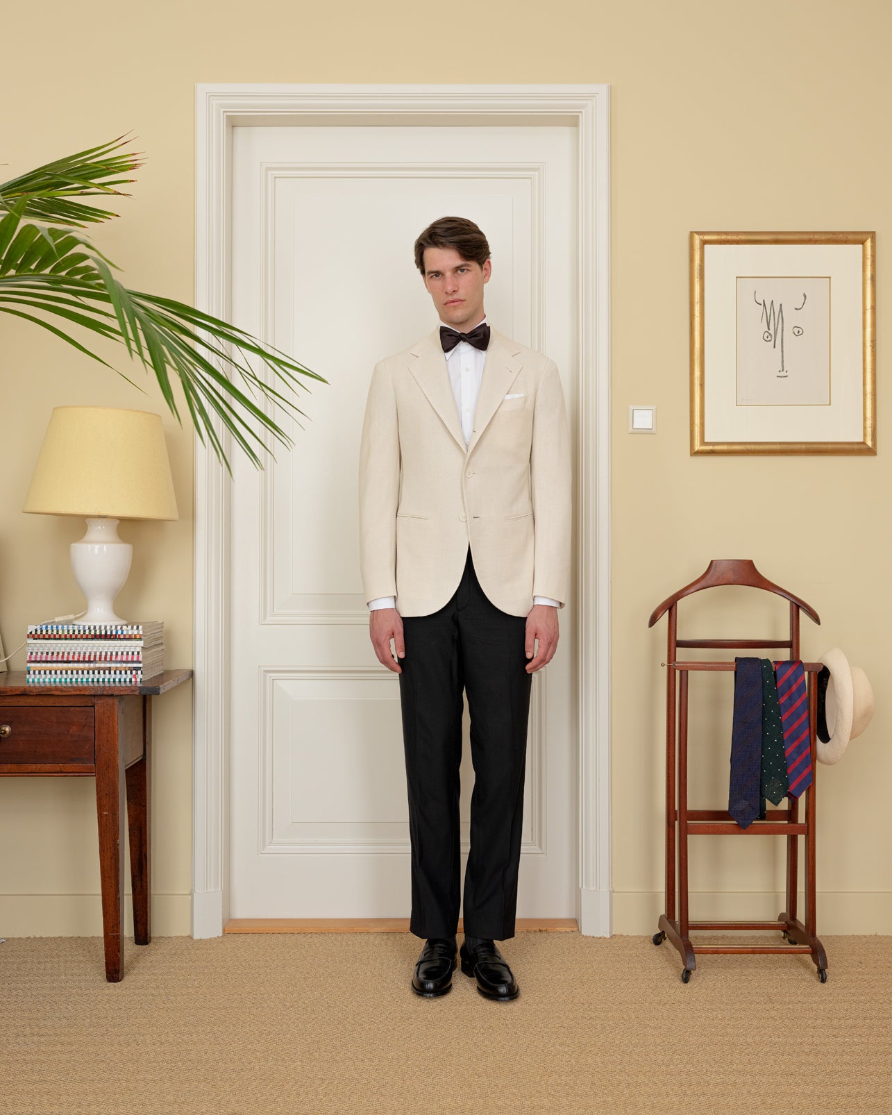 Man wearing a cream silk dinner jacket, black tuxedo trousers, white shirt and black bow tie