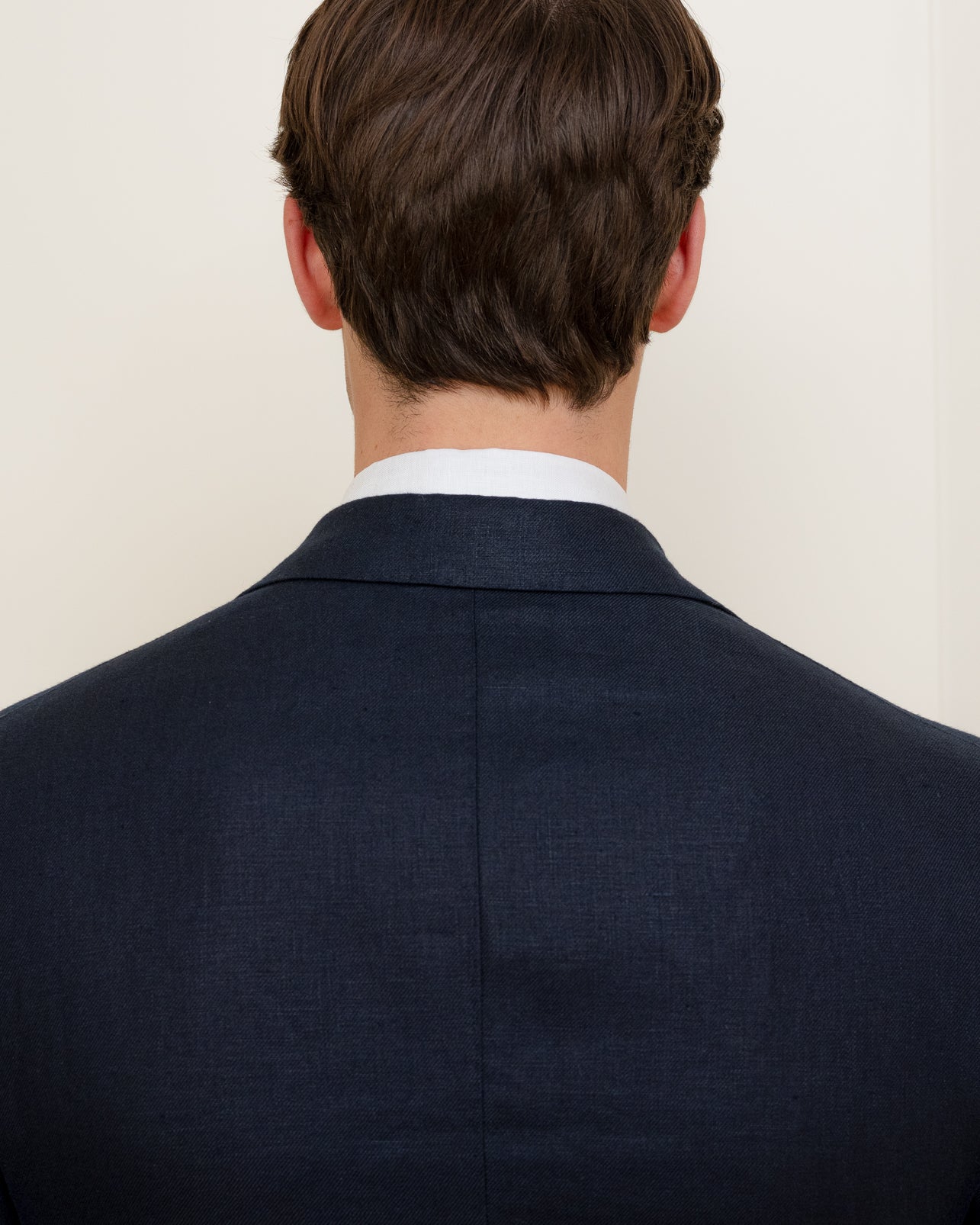 The back of a man wearing a navy linen suit and white shirt