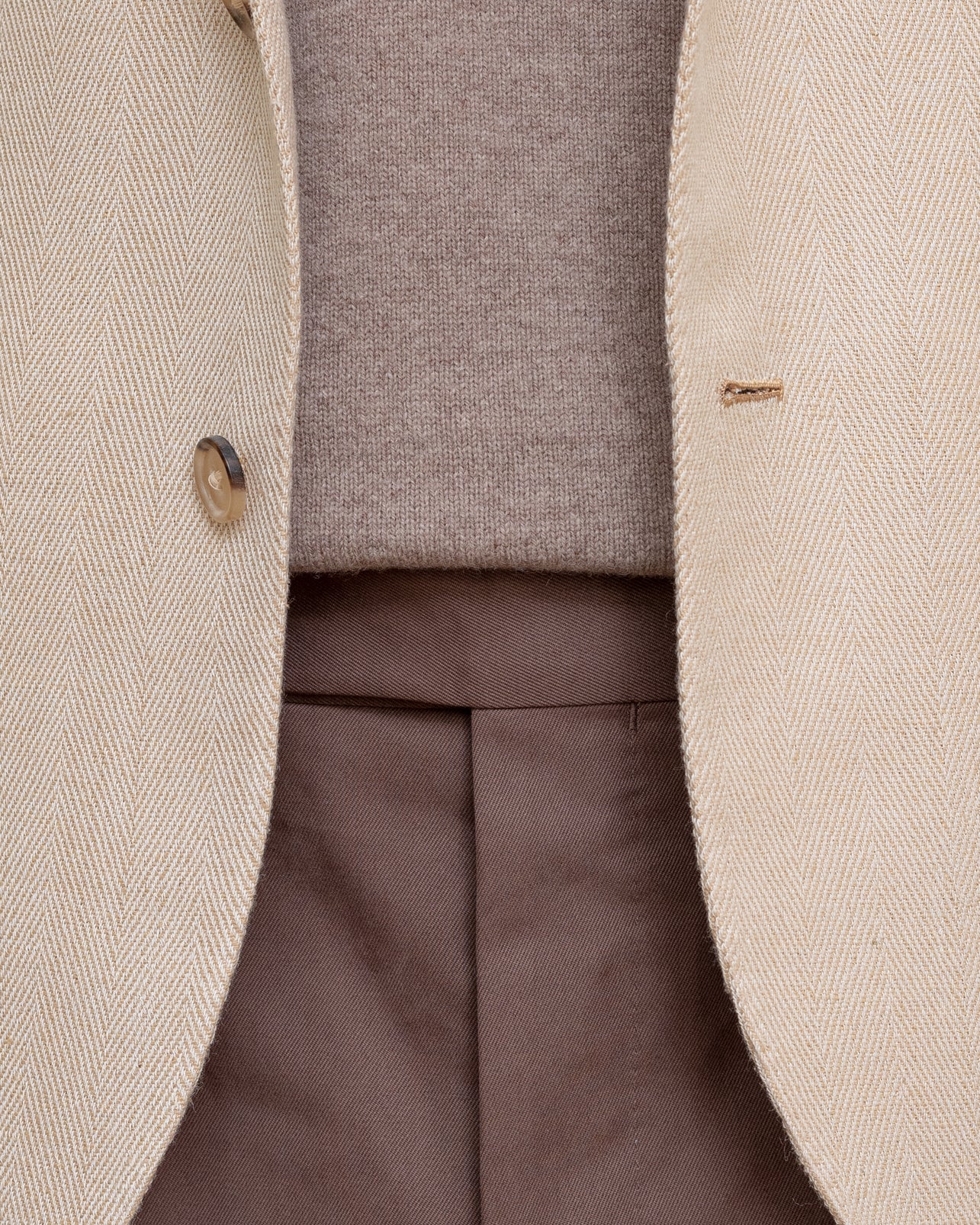 Zoom image of a man wearing a beige herringbone silk sport coat, tobacco cotton drill trousers and a light brown crewneck sweater
