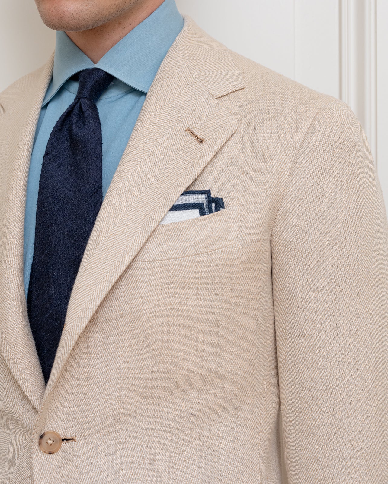Man wearing a light brown silk herringbone sport coat, denim dress shirt and navy shantung silk tie